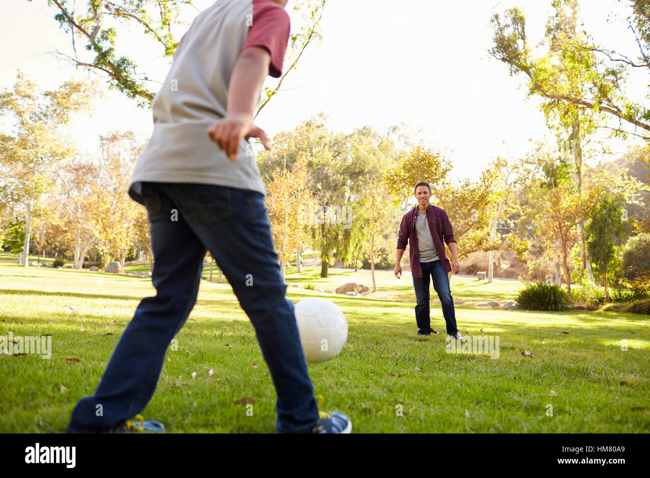 Seven year old boy kicking football to his dad in park, crop Stock Photo