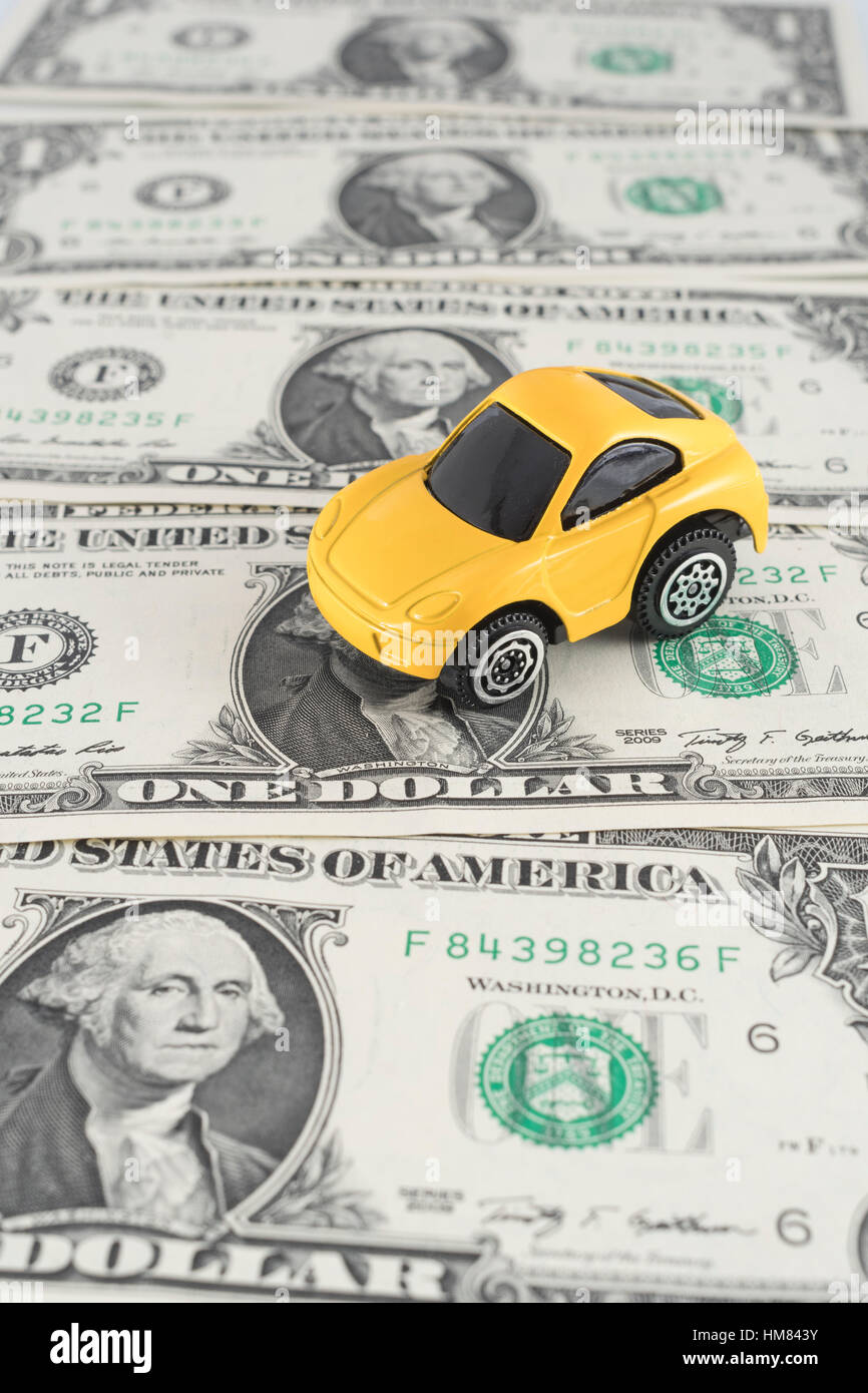 Small yellow toy car on US 1 Dollar / 1 $ bills. As metaphor for the cost of motoring and petrol in the US. Stock Photo