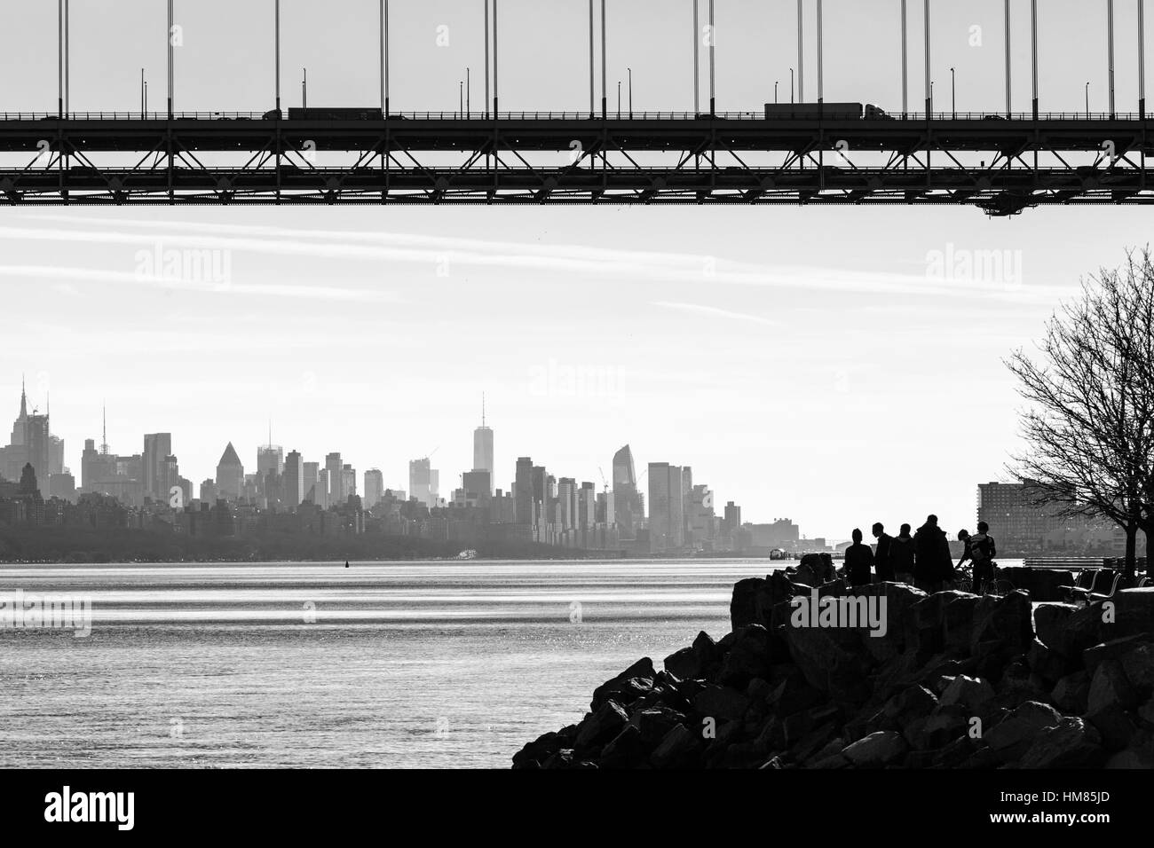 The George Washington Bridge and New York Skyline are seen from Fort Lee Historic Park. The silhouettes of people enjoying the view are on the right. Stock Photo