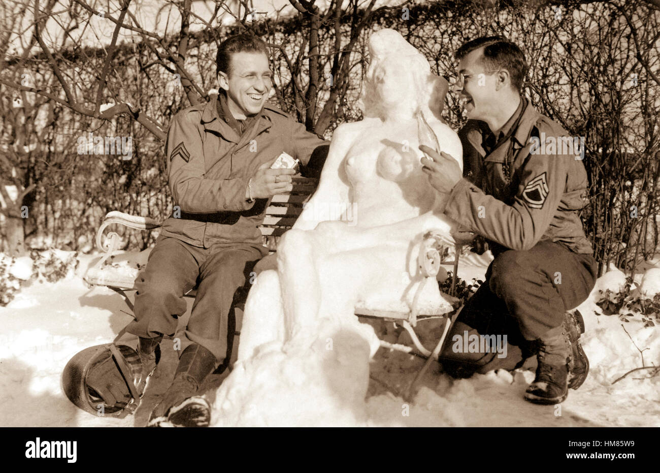Cpl. Bernard Butnik, Cleveland Heights, Ohio, and Sgt. Richard Goodbar, Russellville, Ark., offer 'Anges' their snow woman, cigarettes and a 'coke.'  European theater. January 14, 1945. Sgt. G. W. Herold. (Army) NARA FILE #:  111-SC-198675 WAR & CONFLICT #:  893 Stock Photo