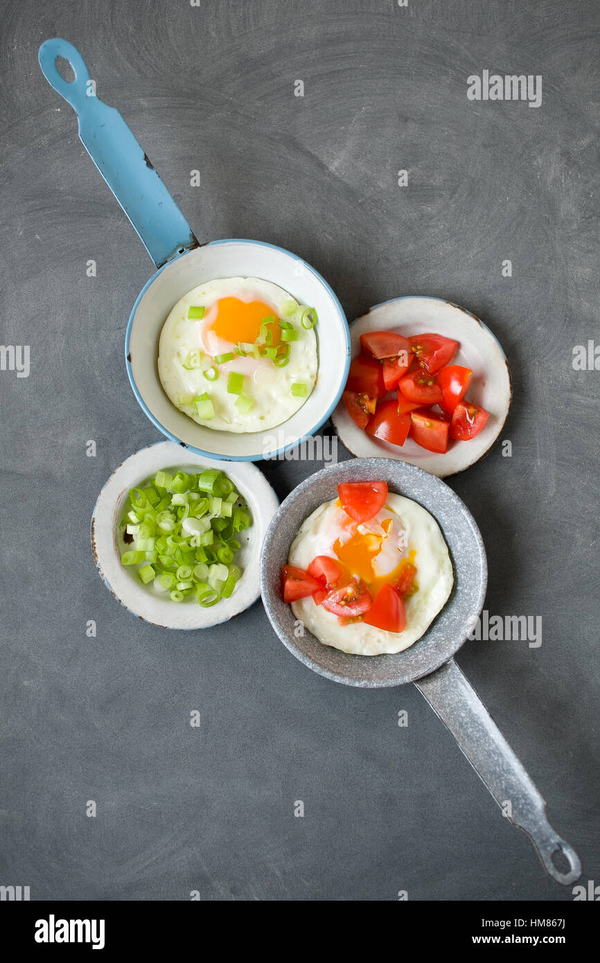 Fried eggs and vegetables on frying pans and plates Stock Photo
