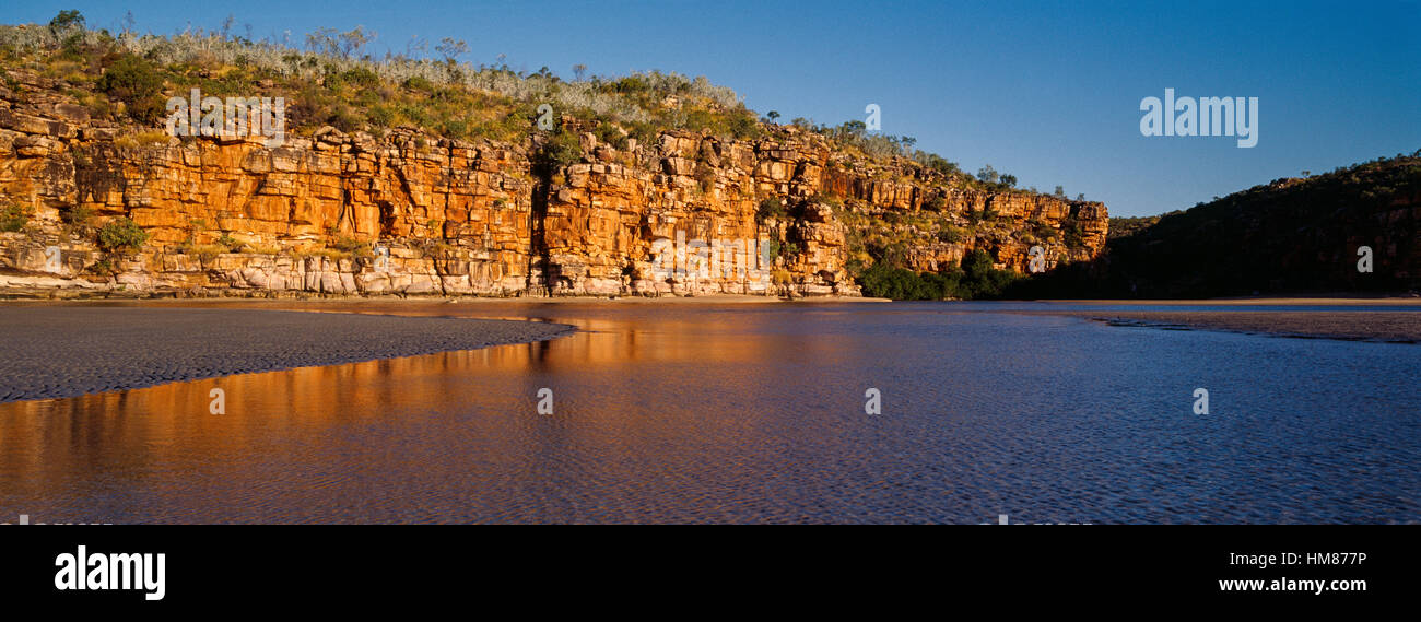 The reflection of orange ochre cliffs in a tidal pool on a beach at sunset. Stock Photo