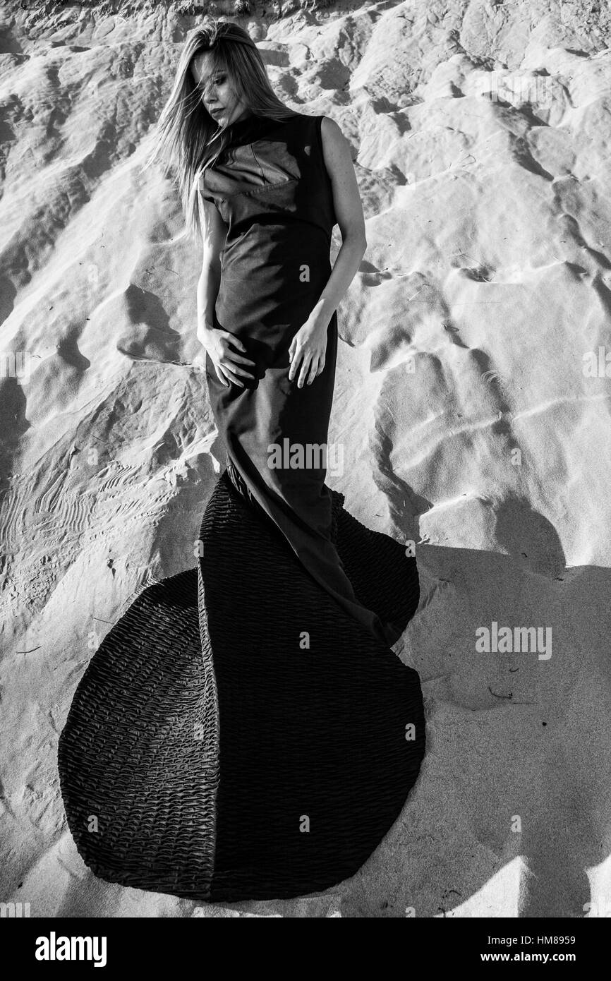 Outdoor Fashion Portrait of Young Adult Woman in Long Black Dress on Sand Dune Stock Photo