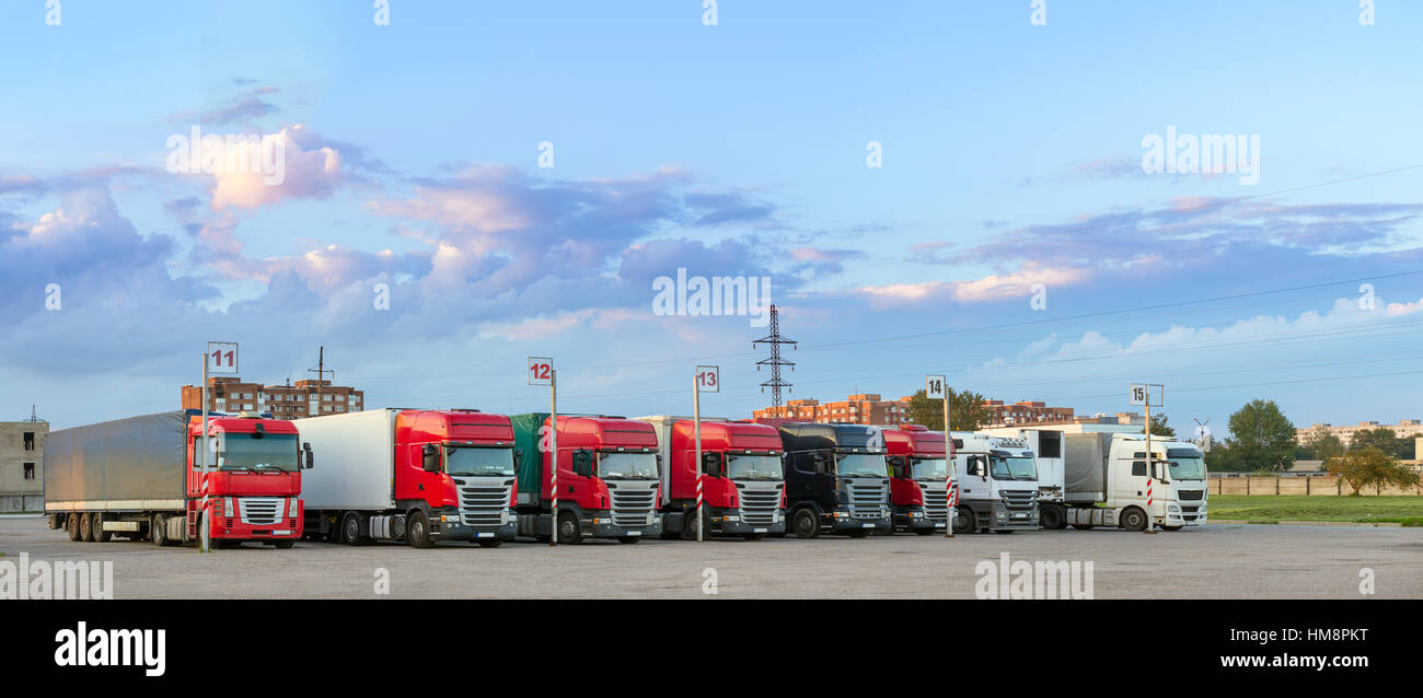 Heavy trucks with trailers loaded with merchandise, stand in a row on an asphalt car platform. International cargo transportation and logistics. Road  Stock Photo