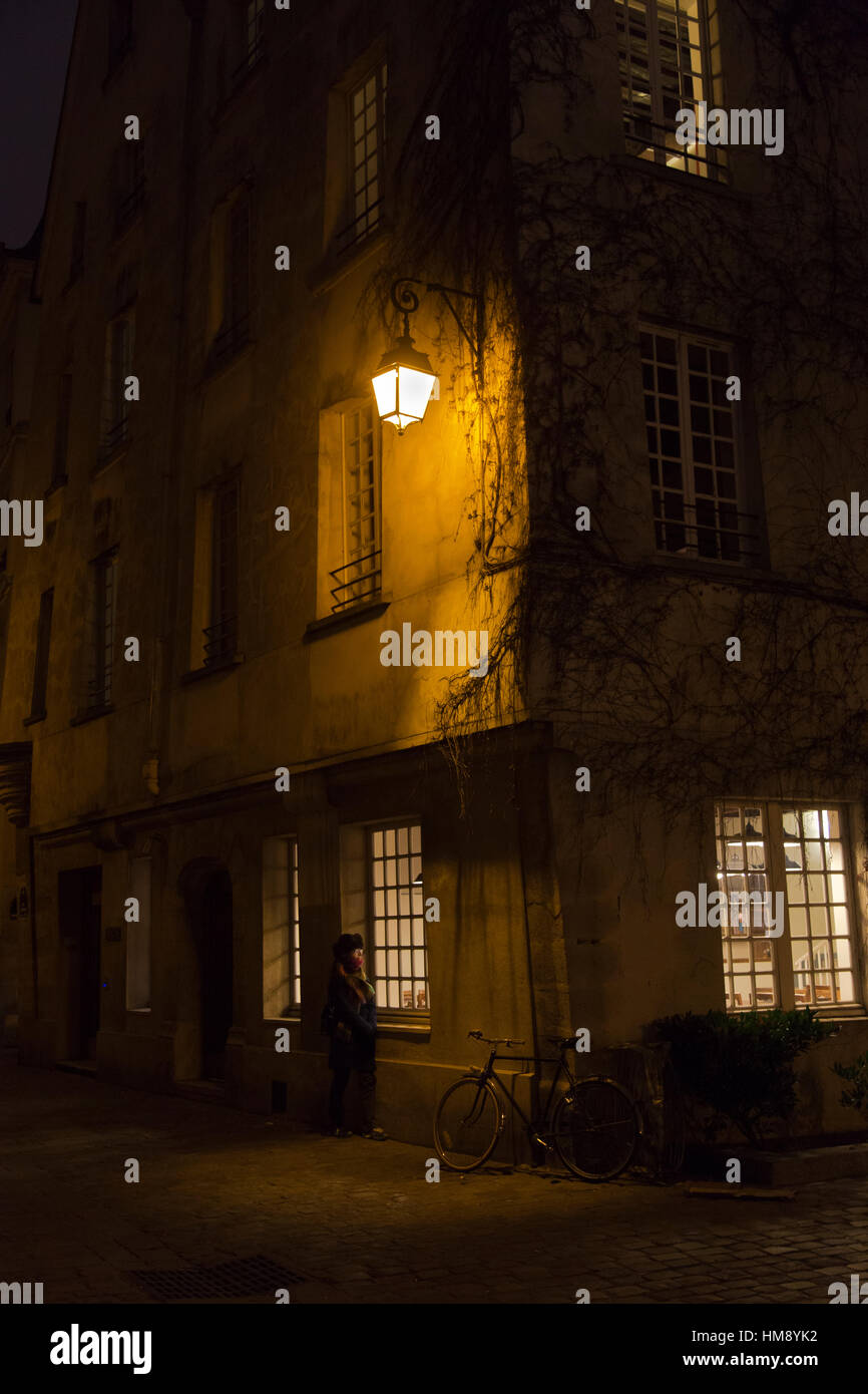 woman by window at night in the 4th arrondissement of Paris in winter Stock Photo