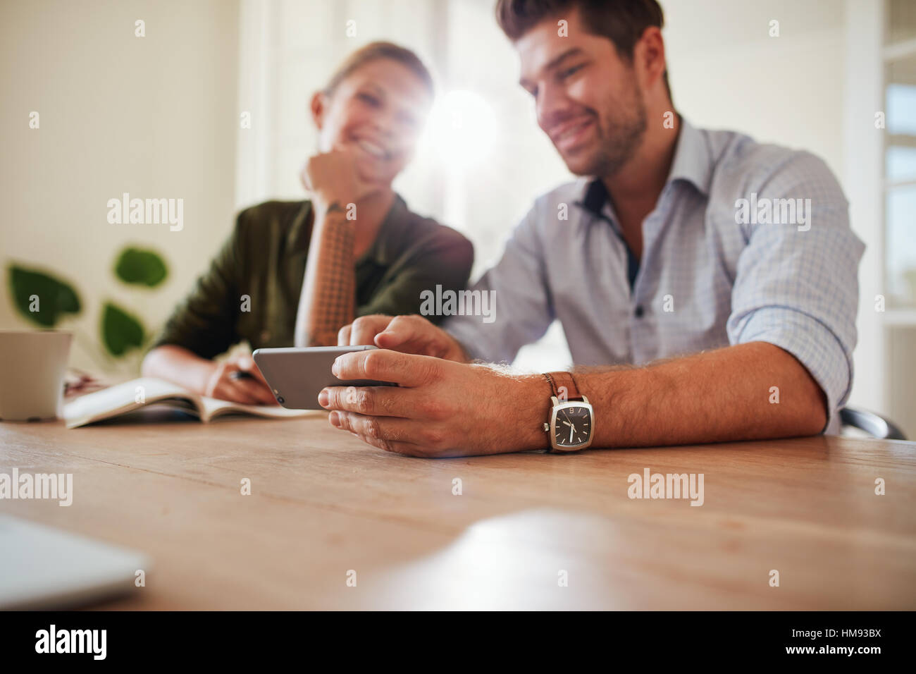 Shot of young couple at table using cellphone at home. Focus on mobile phone in man hands. Stock Photo