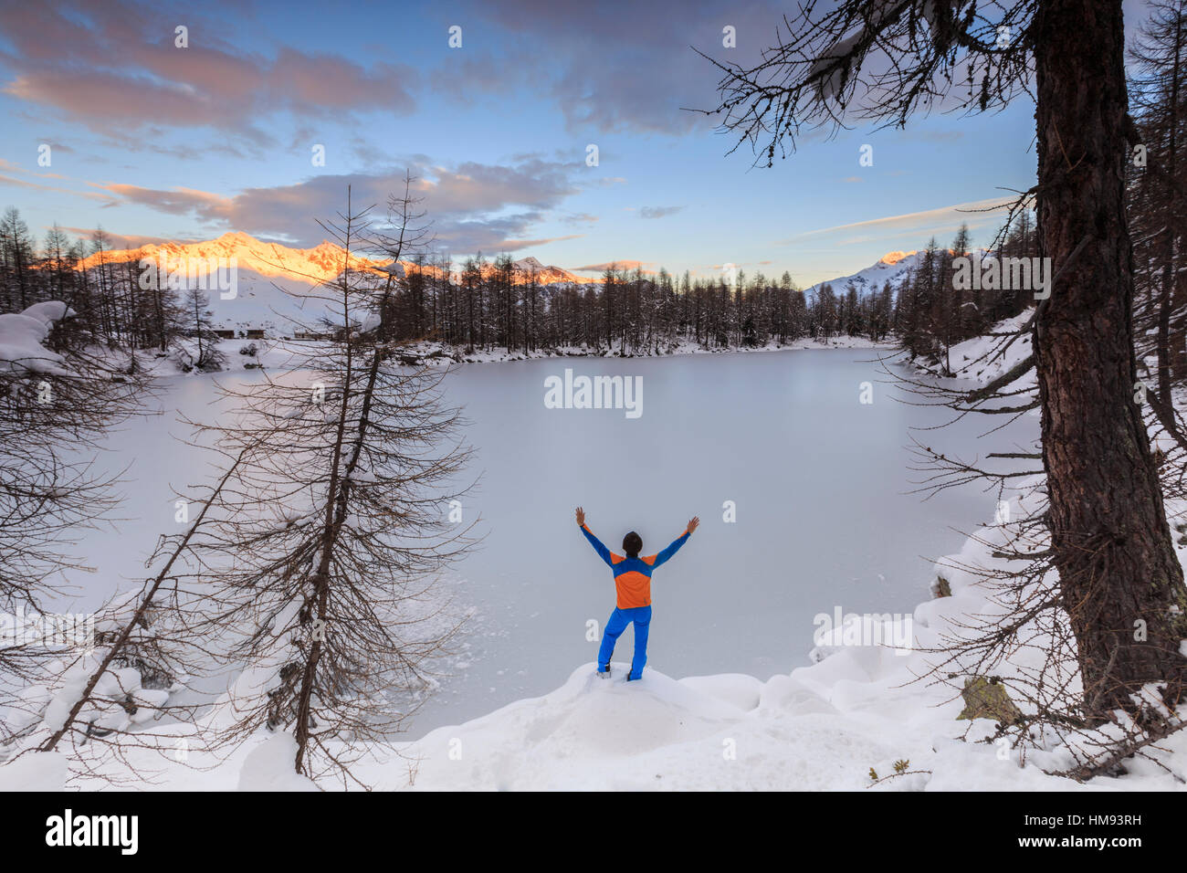 Hiker admires Lago Azzurro completely frozen at dawn, Spluga Valley, Province of Sondrio, Valtellina, Lombardy, Italy Stock Photo