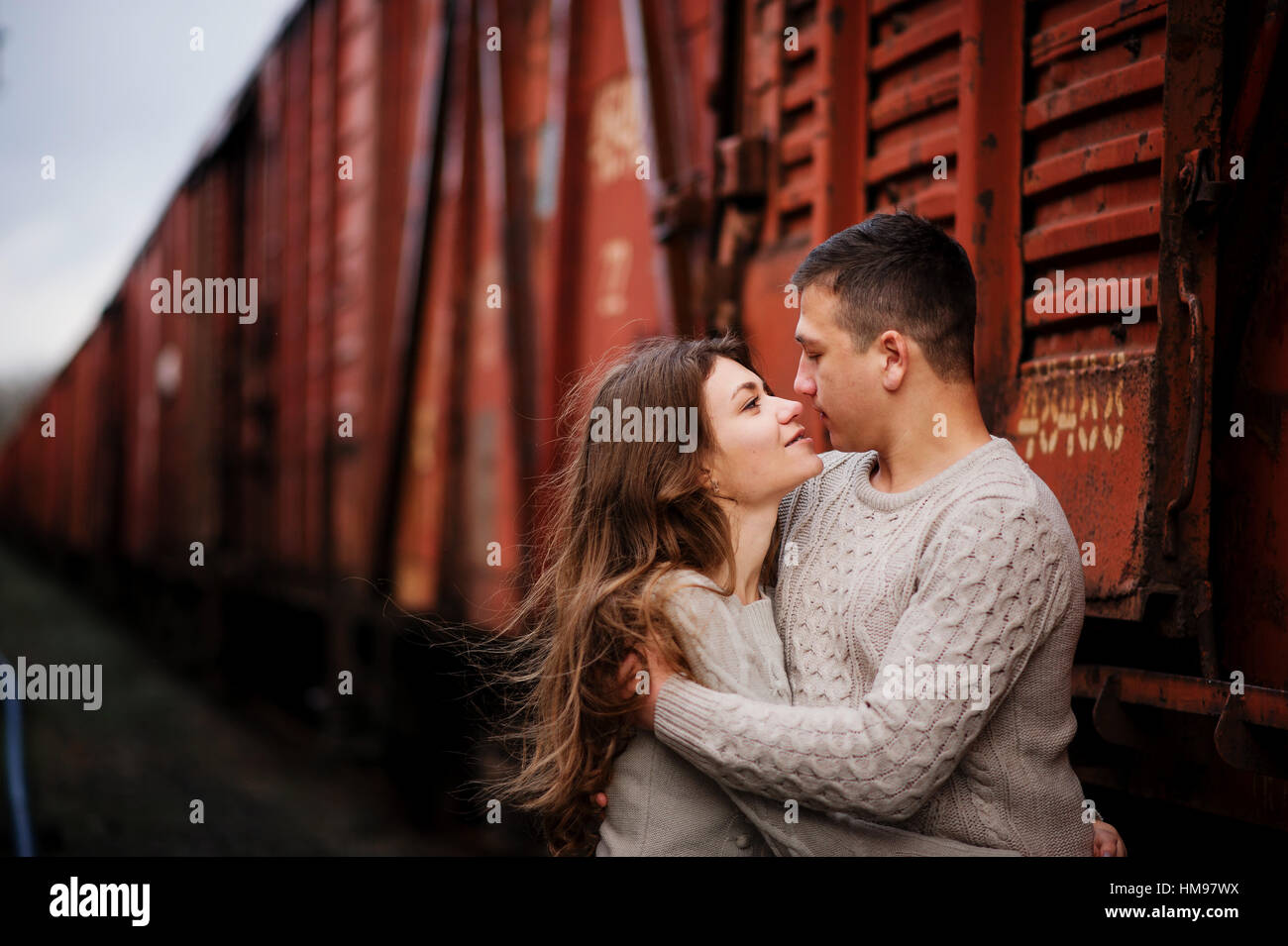 Hugging Freight Young couple wearing on tied warm sweaters hugging in love at railway ...