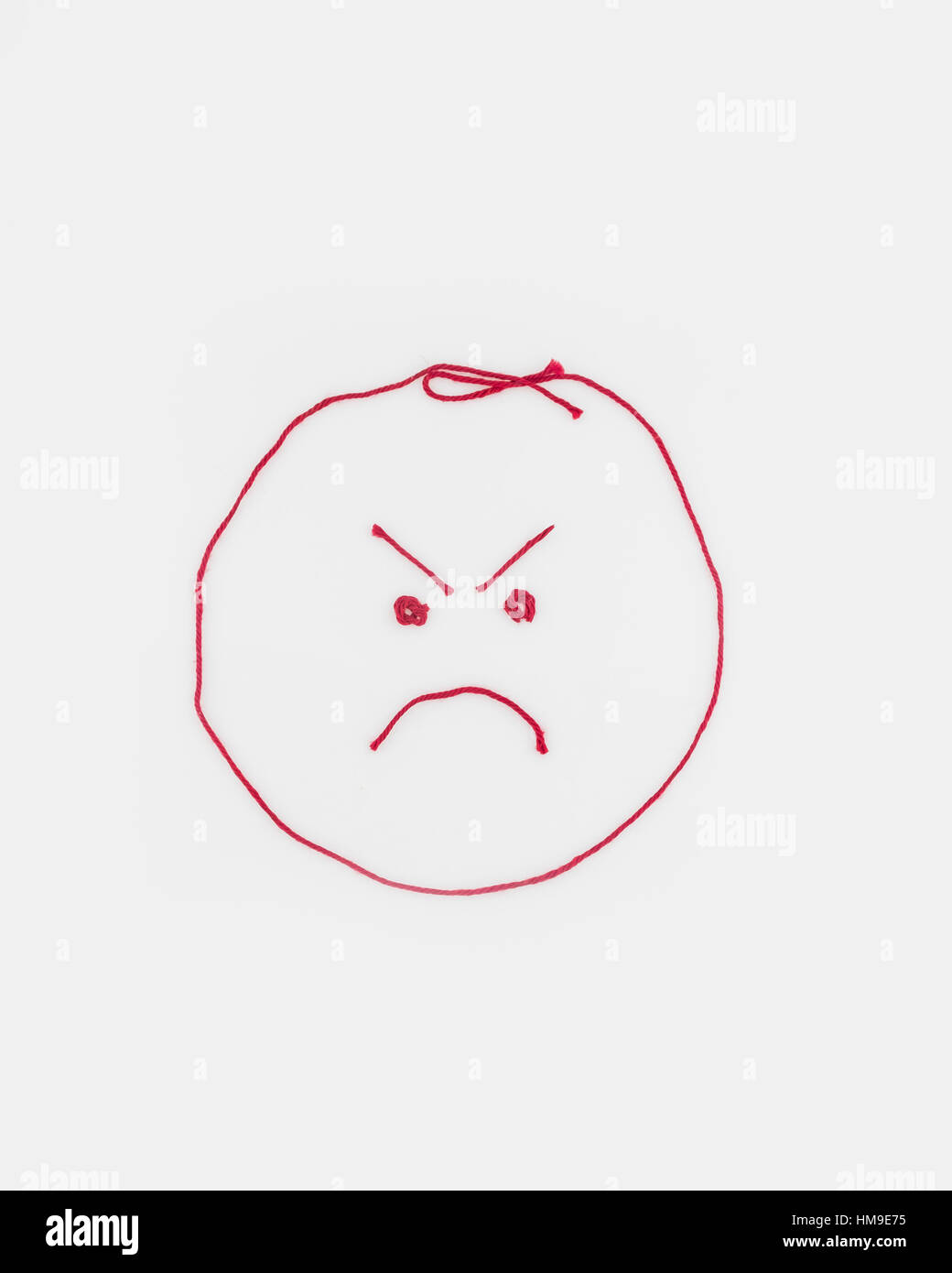 Concept, conceptual. An angry face shaped from red yarn. Cutout. Stock Photo