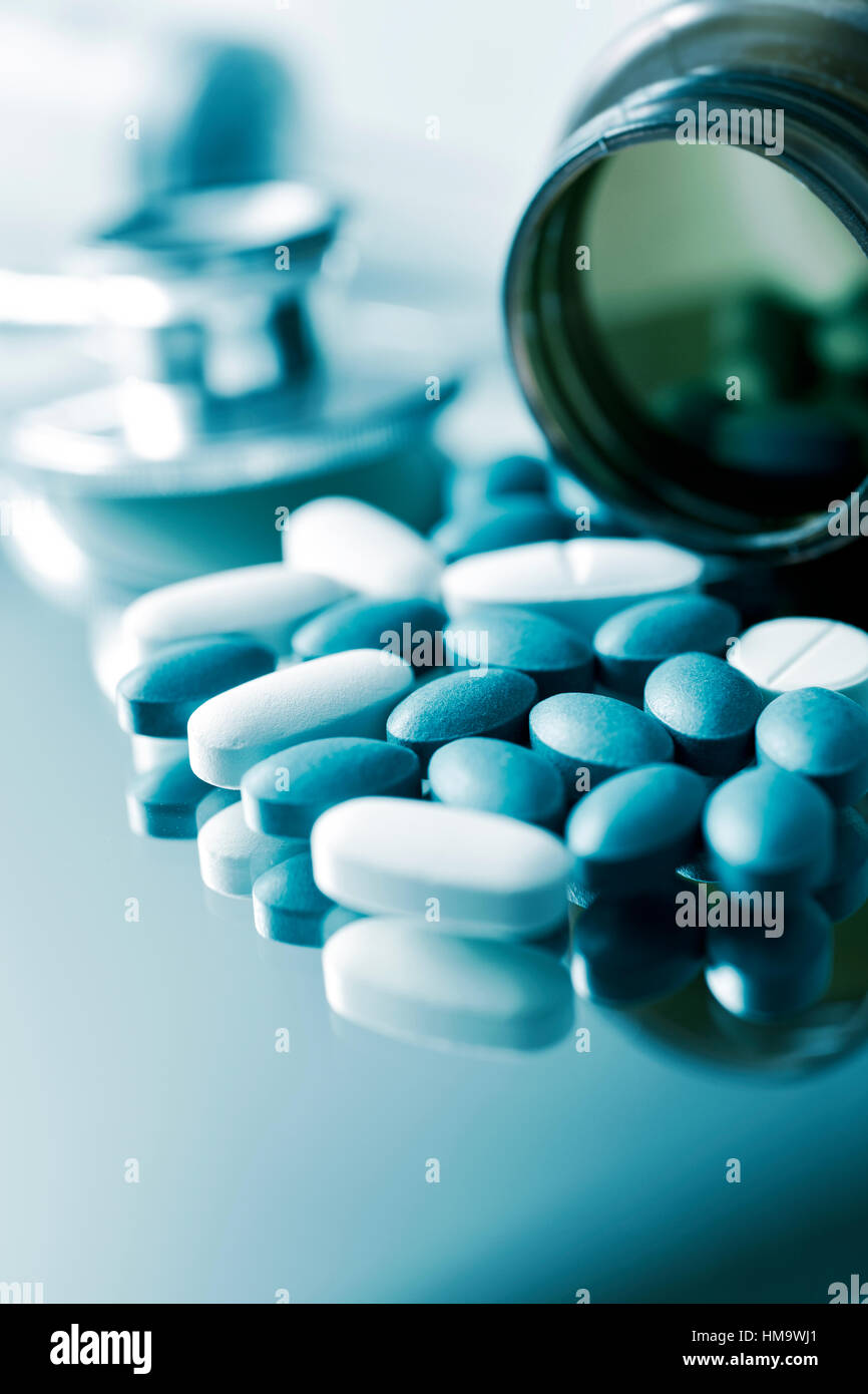 closeup of the desk of a doctors office with a bottle with pills in the foreground and a stethoscope in the background Stock Photo