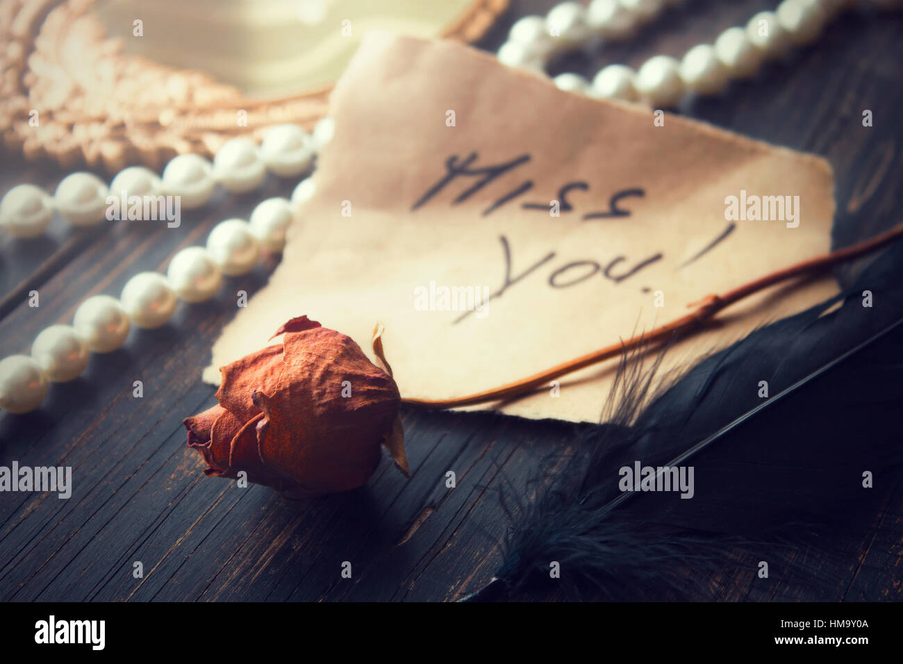 Love note on an old parchment paper with words miss you on it, decorated with old withered rose and some pearls in background Stock Photo