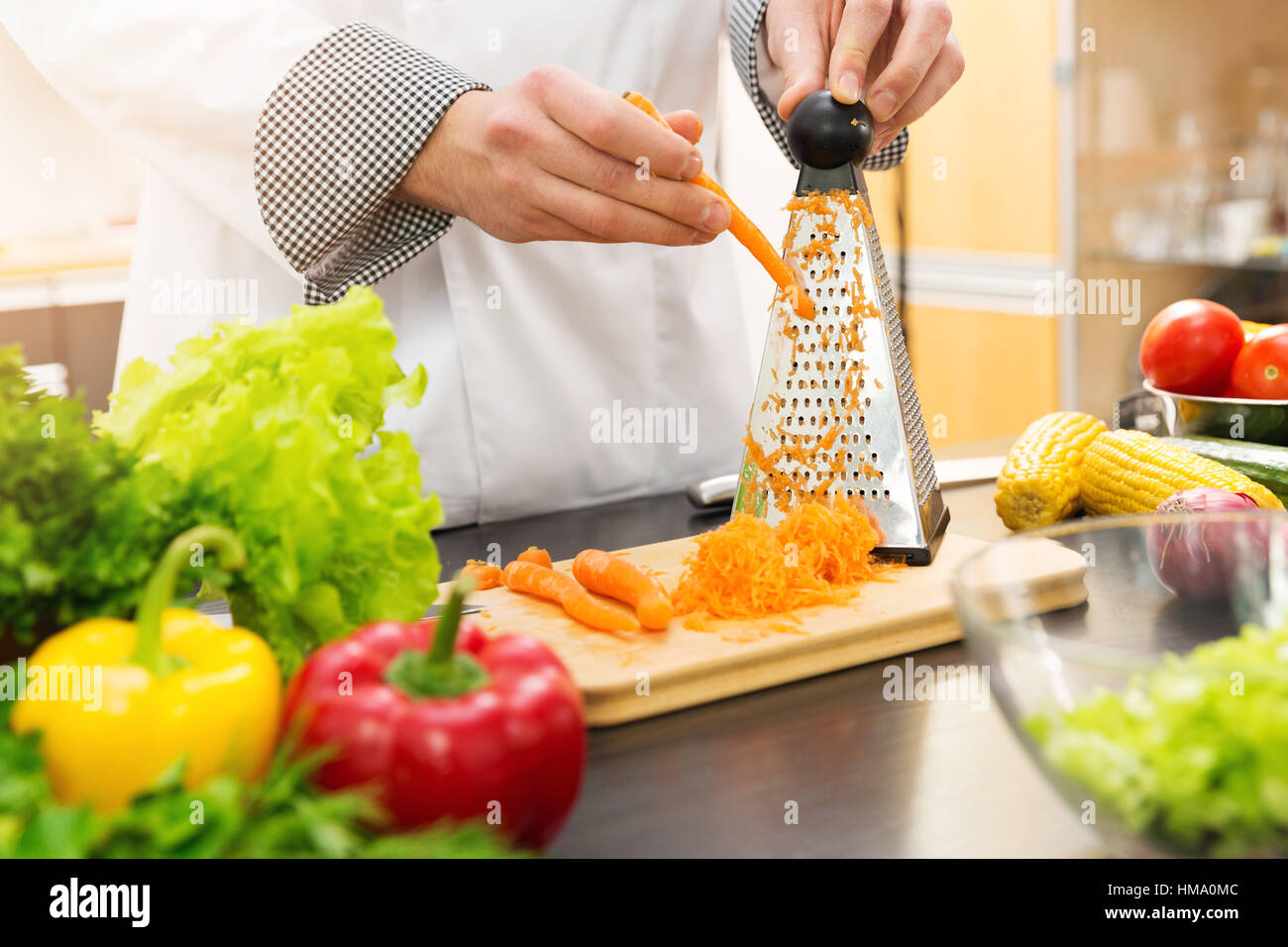 chef shredding carrots with grater in kitchen Stock Photo