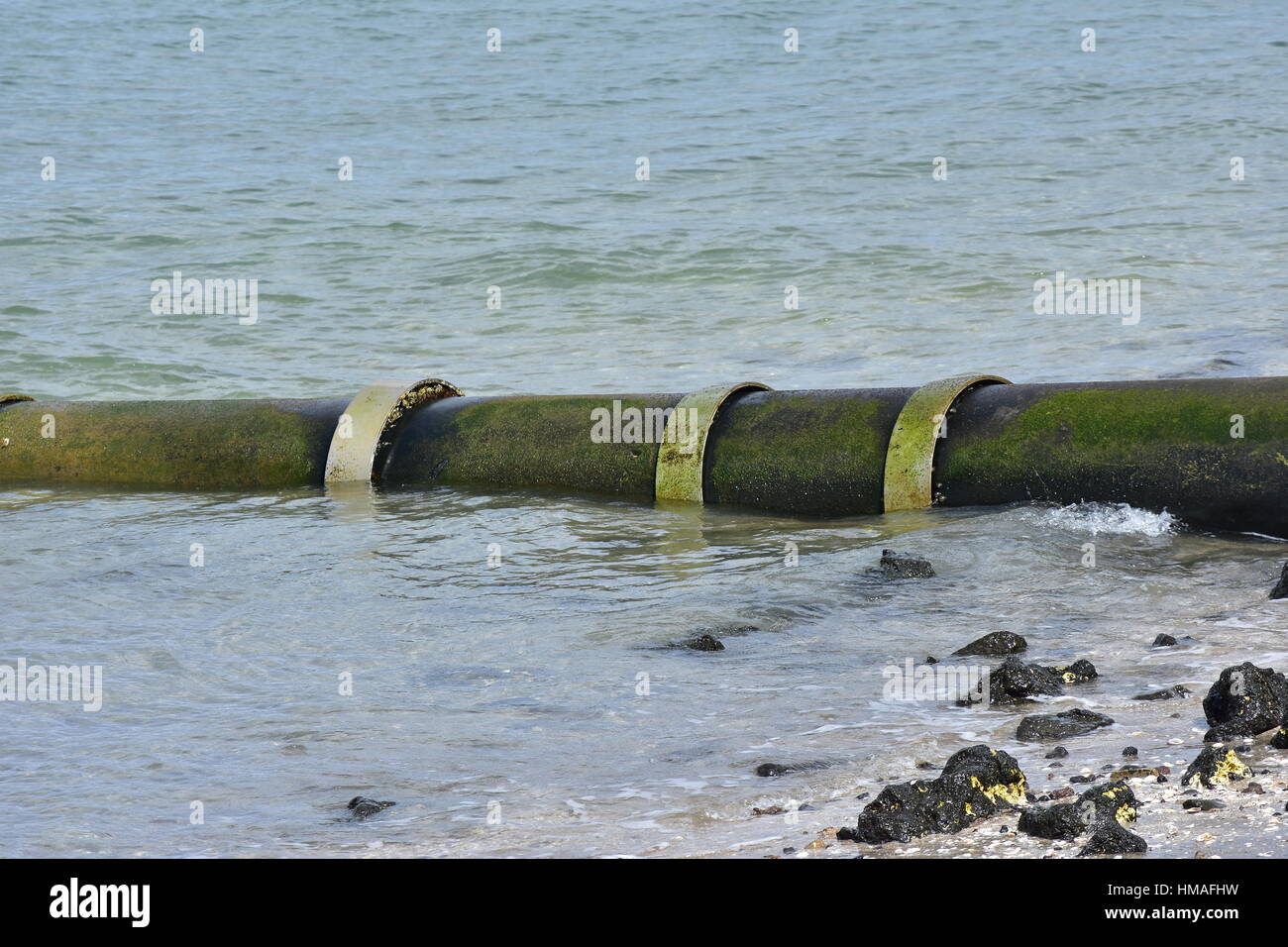 Large bore metal pipe entering sea at low angle on sandy shore with