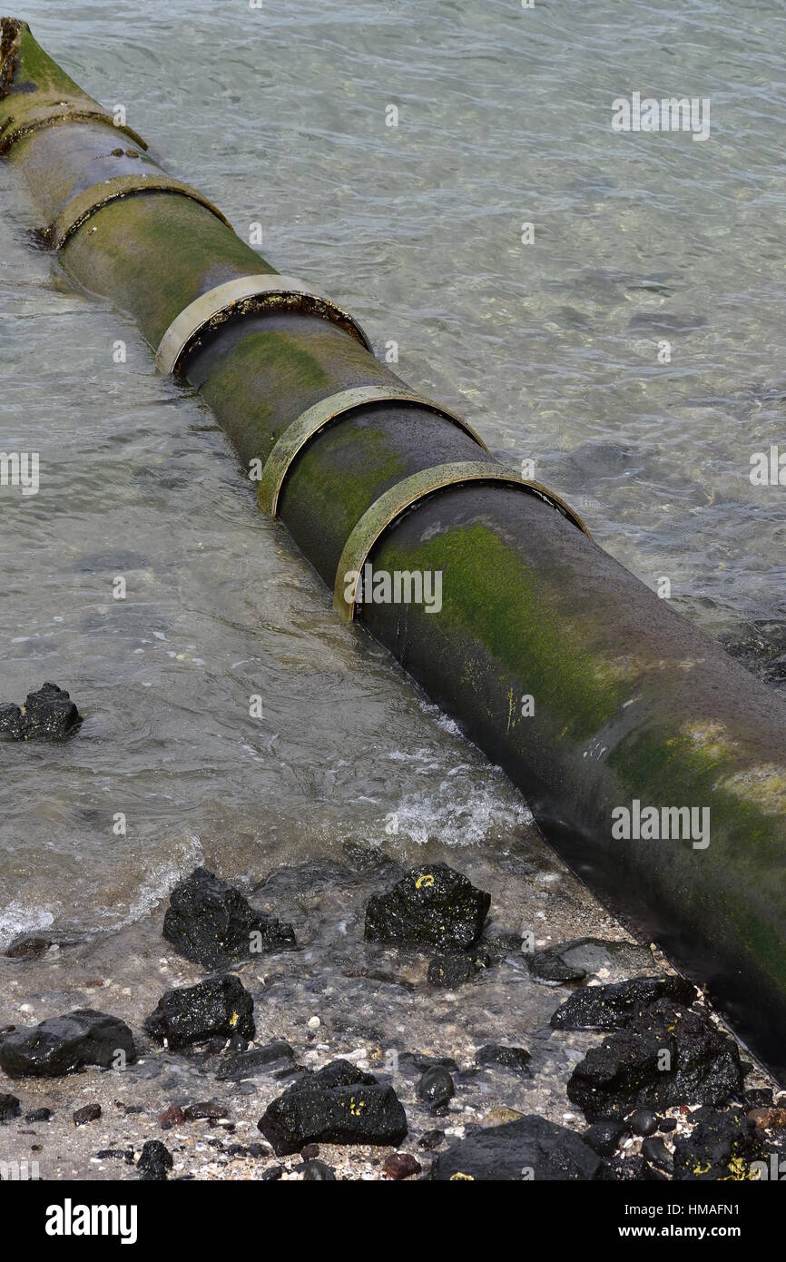 Large bore metal pipe entering sea at low angle on sandy shore with
