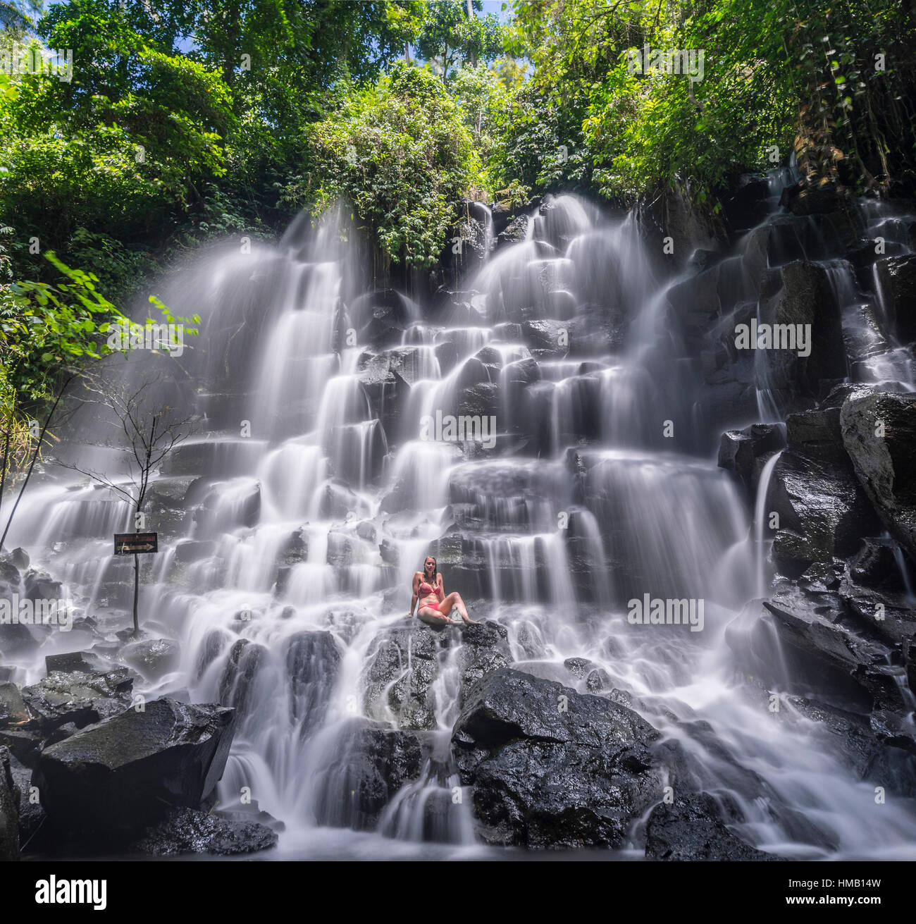 Woman sitting on rock, waterfall, Air Terjun Kanto Lampo, near Ubud, Bali, Indonesia Stock Photo