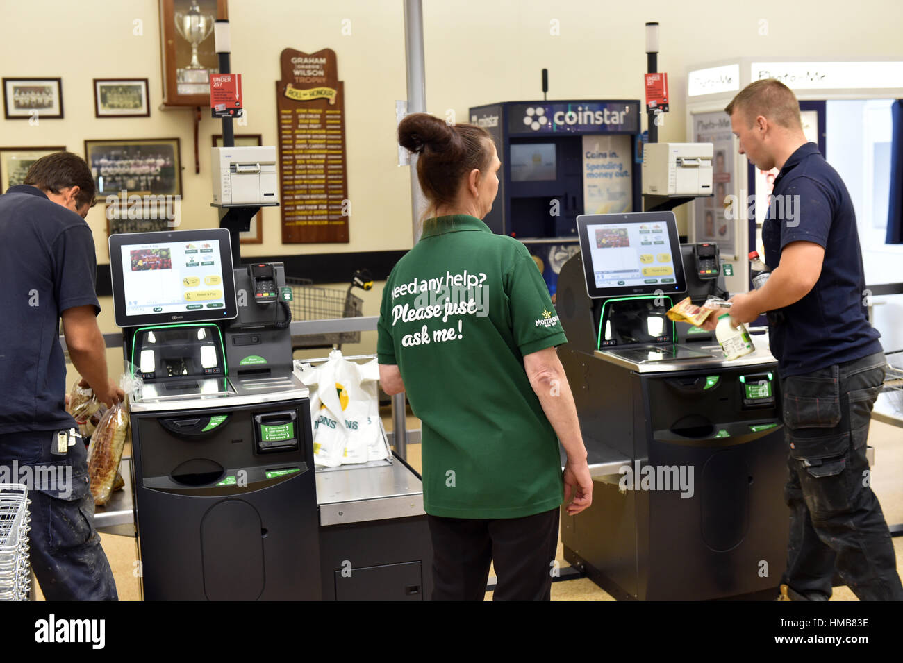 Shop Assistant helps customers on the self checkout in a supermarket Stock Photo