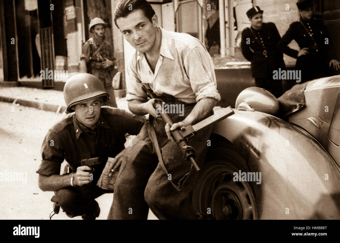 American officer and French partisan crouch behind an auto during a street fight in a French city, ca.  1944. (Army) Exact Date Shot Unknown NARA FILE #:  111-SC-217401 WAR & CONFLICT BOOK #:  1055 Stock Photo
