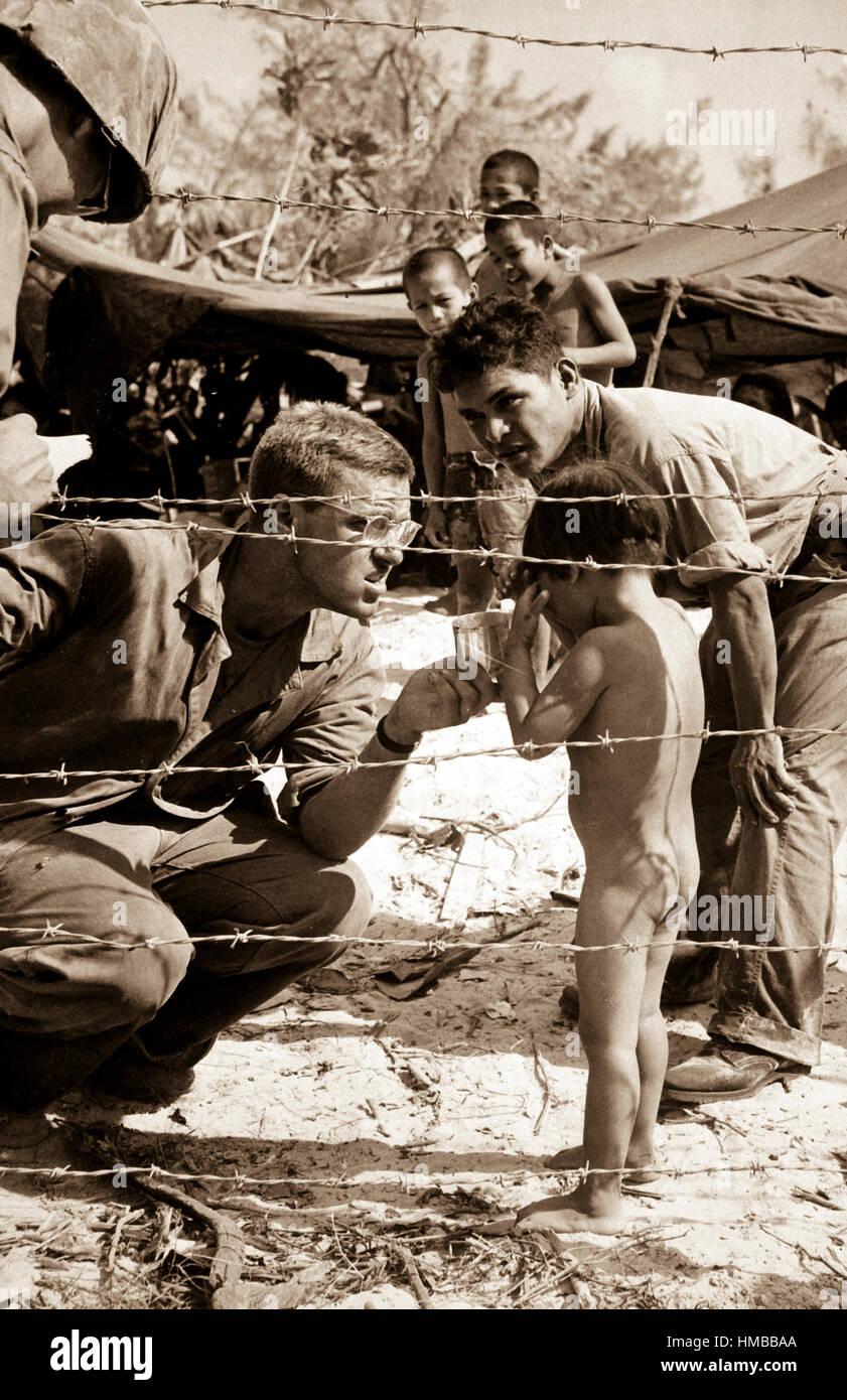 Marines try to soothe a crying child by offering a shiny rations tin.  Children are sheltered with their families in a camp set up for refugees from battle areas by U.S. Marine Civil Affairs authorities on Saipan.  July 1944.  PhoM1c. Ted Needham.  (Coast Guard) Exact Date Shot Unknown NARA FILE #:  026-G-2528 WAR & CONFLICT BOOK #:  1268 Stock Photo
