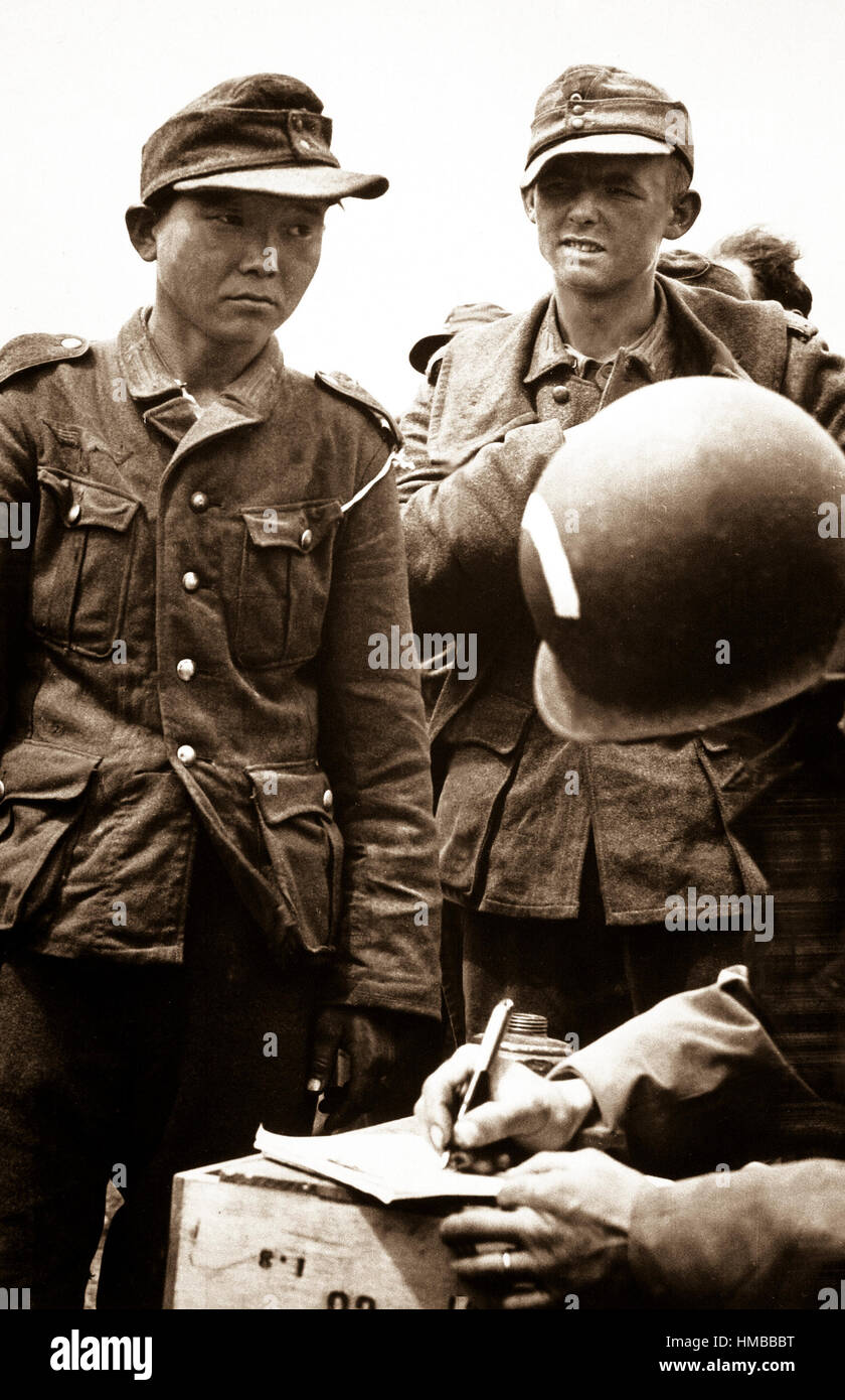 Dismay and loneliness is written on the face of this young Jap, wearing a Nazi uniform, in a roundup of German prisoners on the beaches of France.  The Jap is giving his name and number to an American Army captain.  1944.  (Coast Guard) Exact Date Shot Unknown NARA FILE #:  026-G-2391 WAR & CONFLICT BOOK #:  1286 Stock Photo