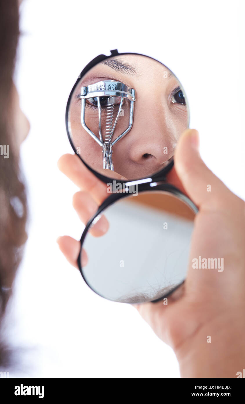 reflection on mirror of girl's eye while curling her eyelashes Stock Photo
