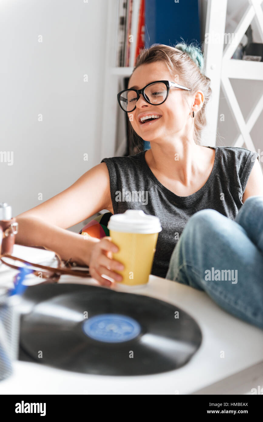 Cheerful relaxed young woman with cup of coffee sitting with legs on ...