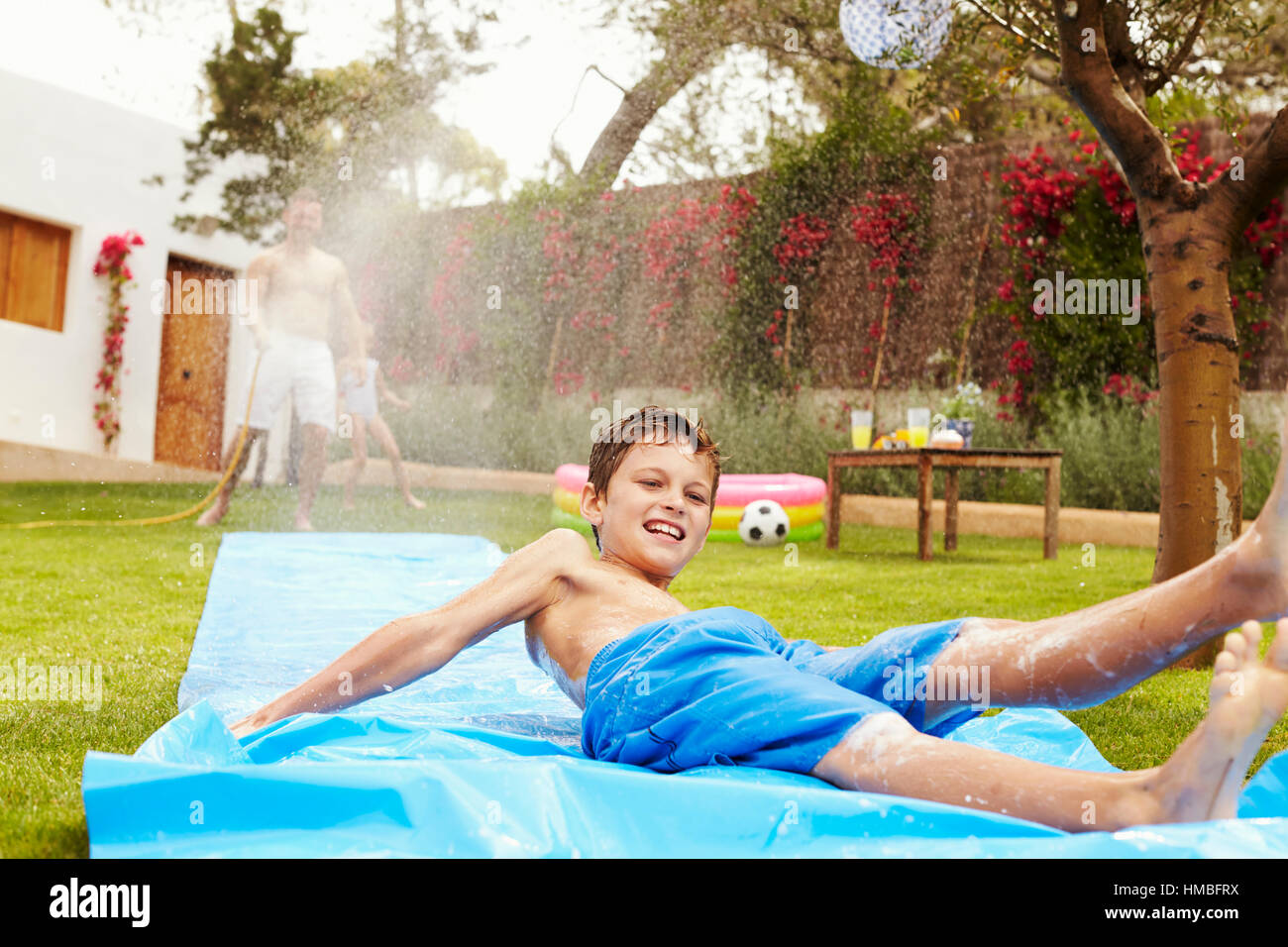Father And Son Having Fun On Water Slide In Garden Stock Photo