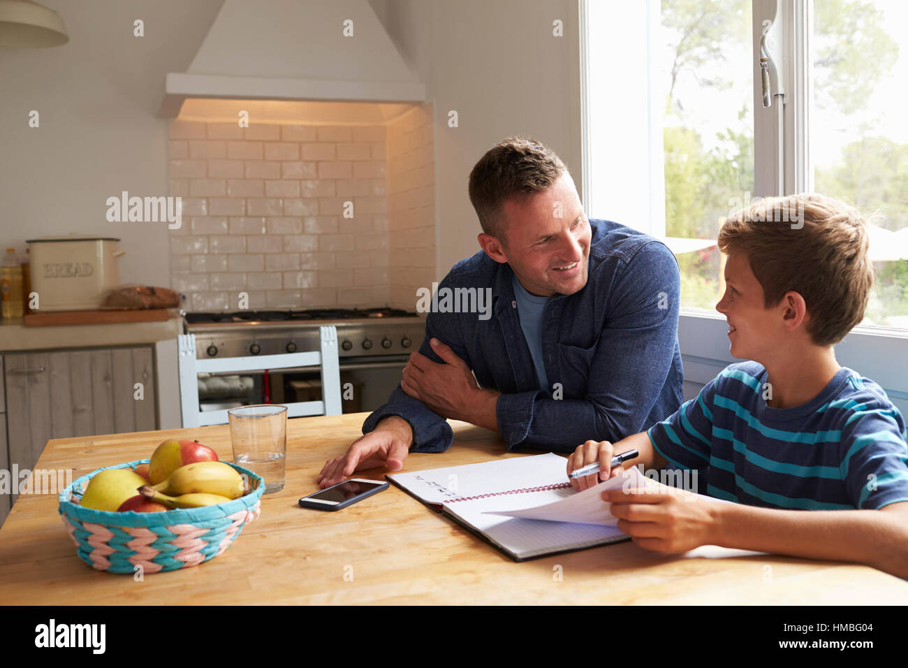 Father Helping Son With Homework Sitting At Kitchen Table Stock Photo ...