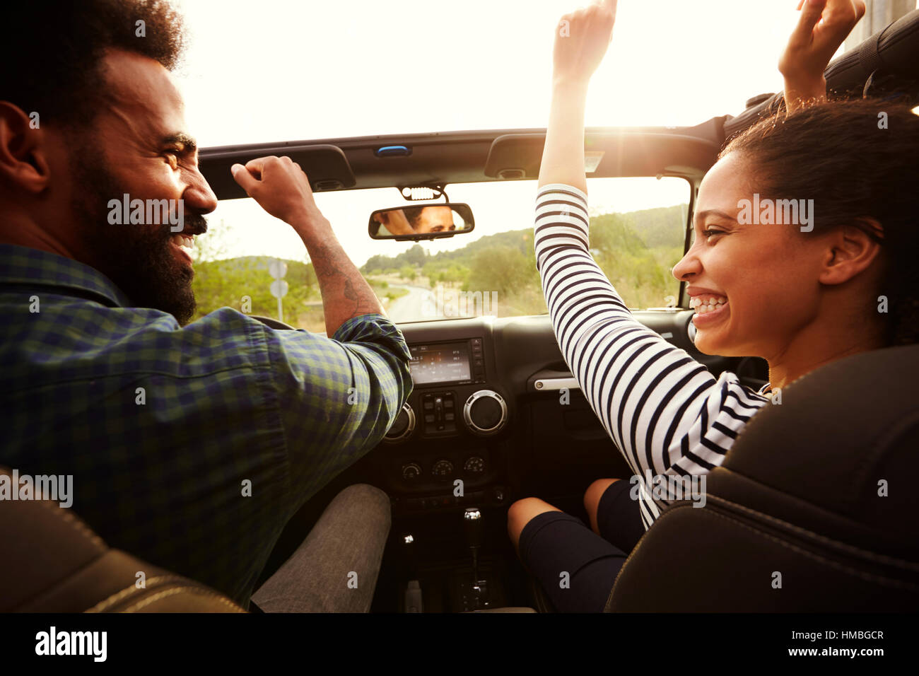 Happy couple driving in their car with arms in the air Stock Photo