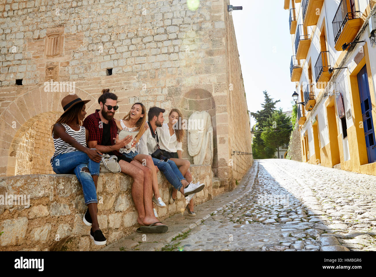 Five friends on holiday sitting on a wall in Ibiza Stock Photo
