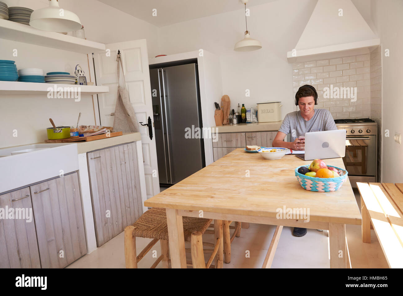 Teenage boy wearing headphones using technology in a kitchen Stock Photo