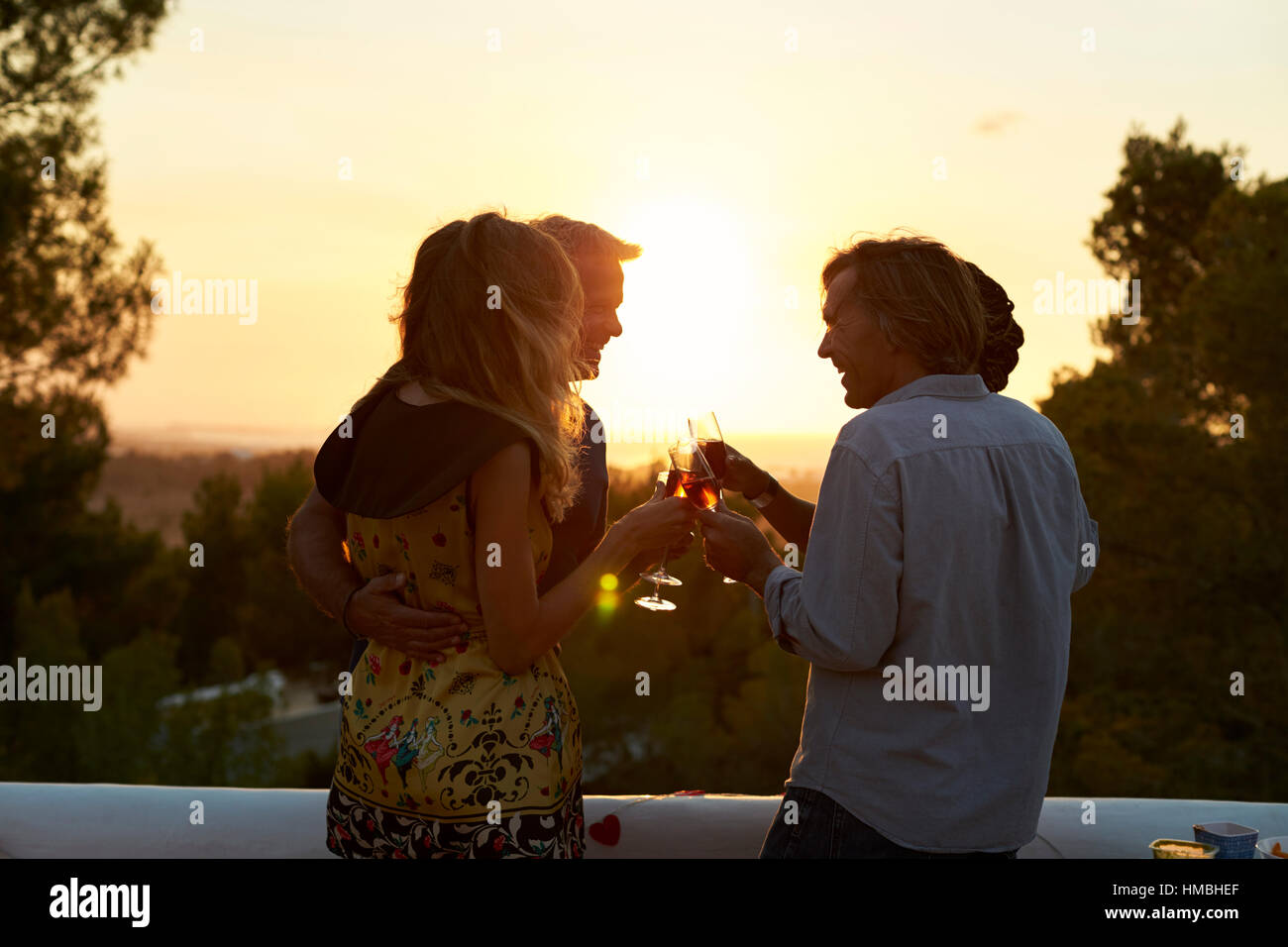 Two couples on a rooftop making a toast at sunset, low light Stock Photo
