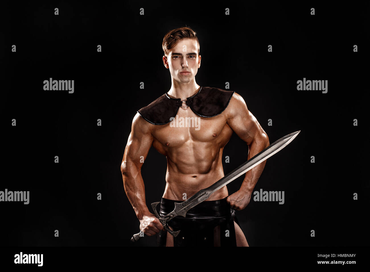 Portrait of handsome muscular gladiator with sword. Isolated. Studio shot. Black background Stock Photo