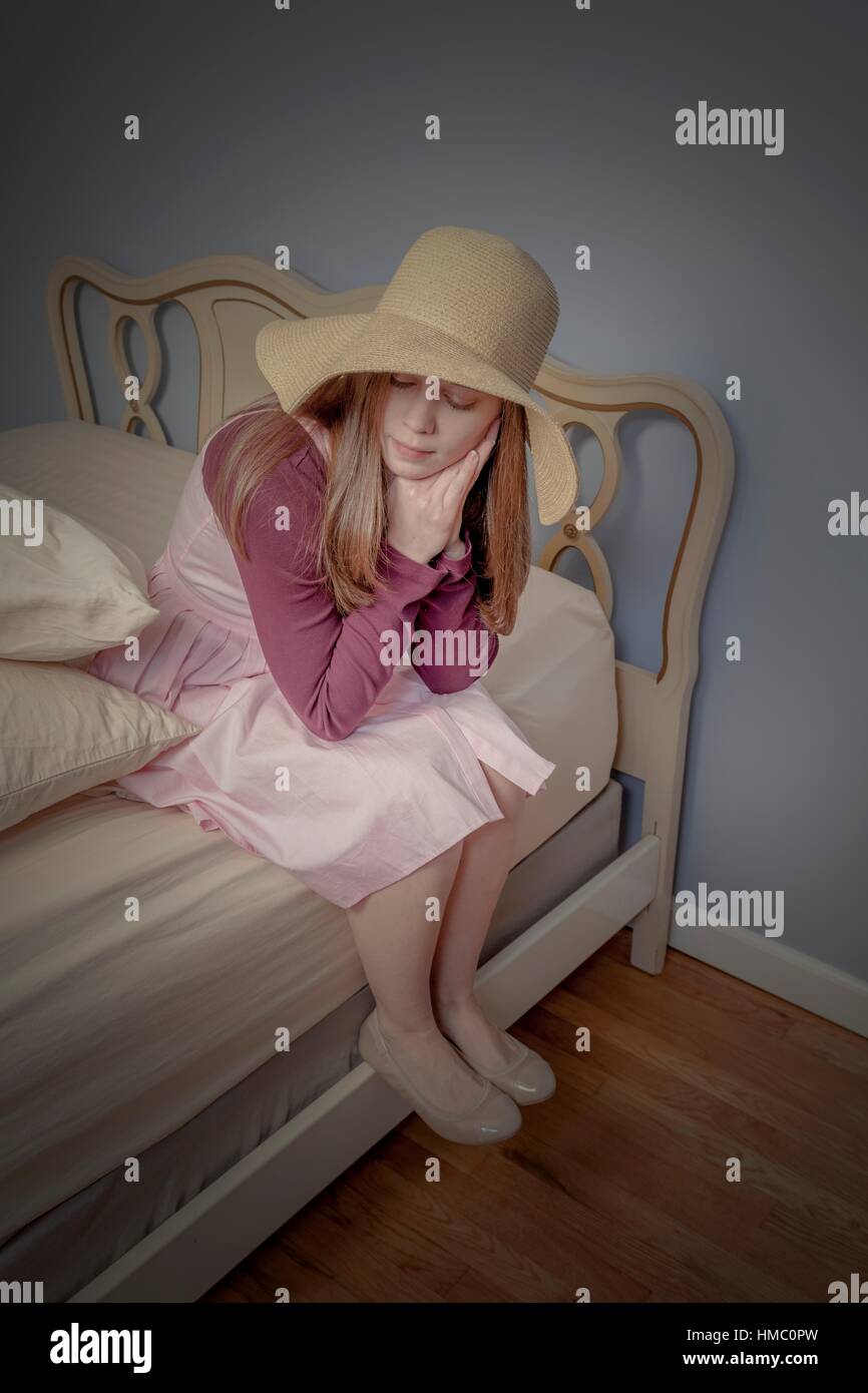 Young woman, wearing a hat, sitting on a bed Stock Photo Alamy