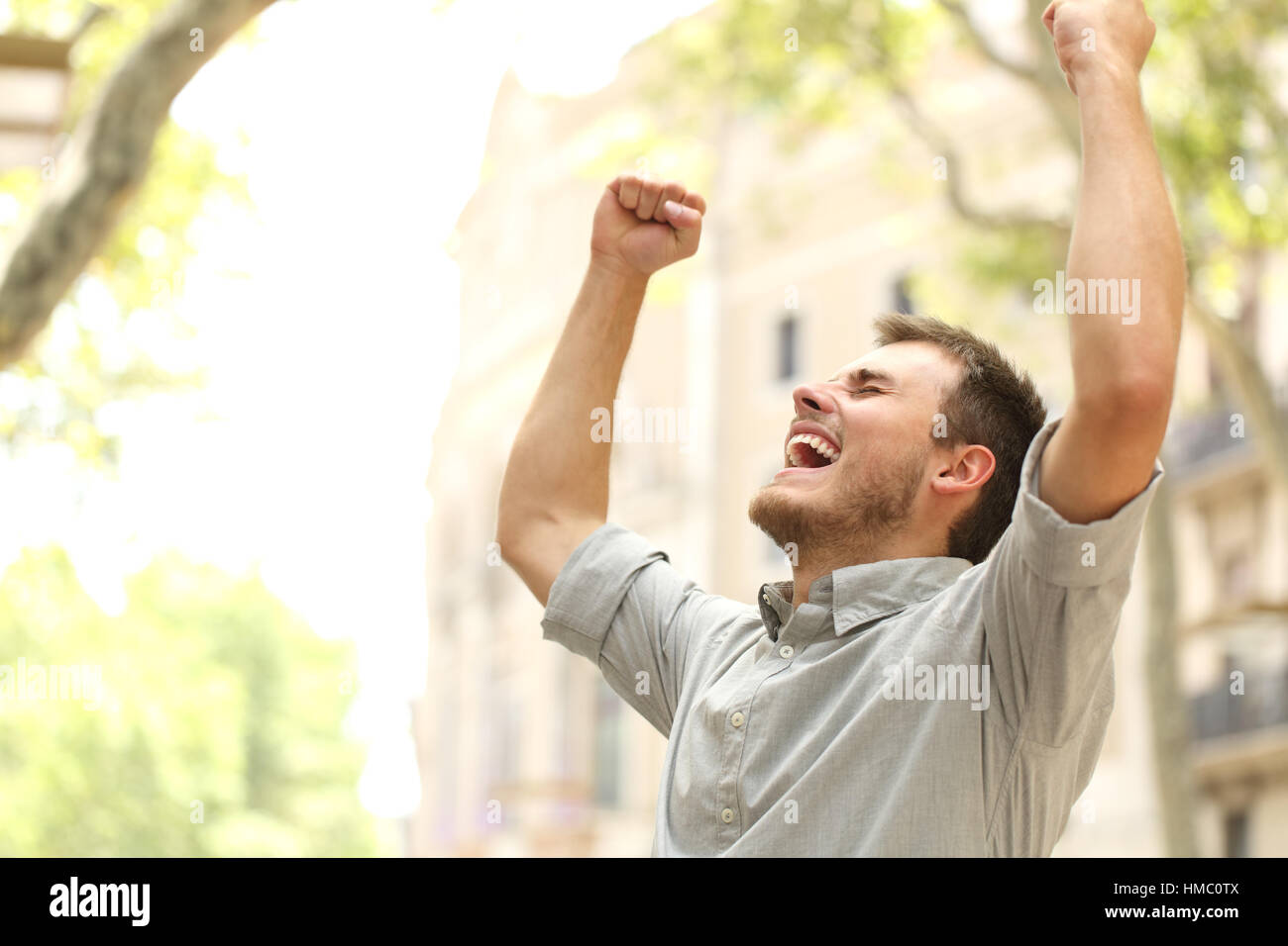 Portrait of an excited man raising arms in the street with buildings in ...