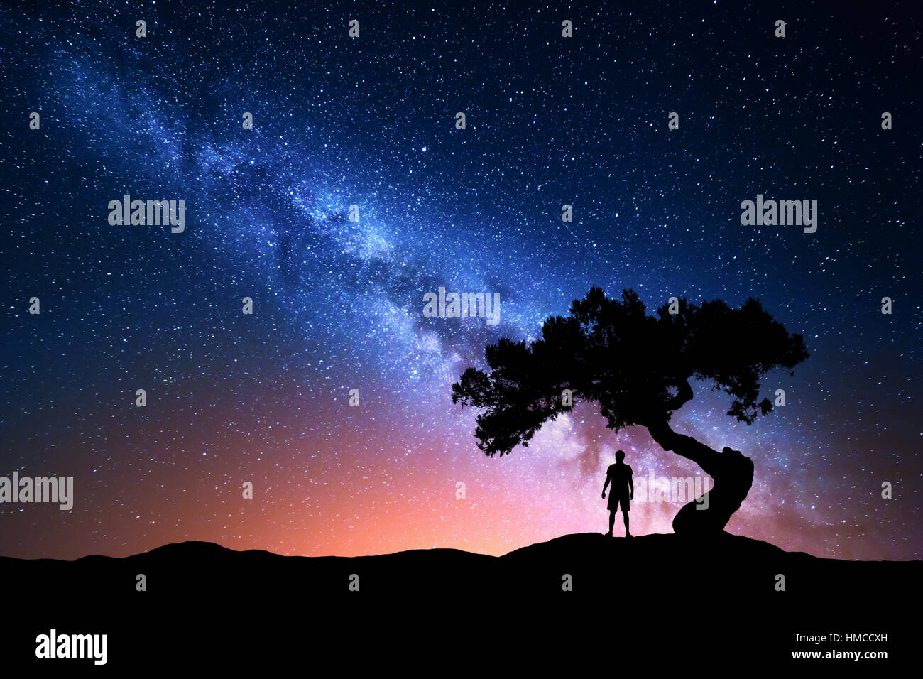 Milky Way. Night sky with stars, old tree and silhouette of a standing alone man on the mountain. Milky way and man Stock Photo