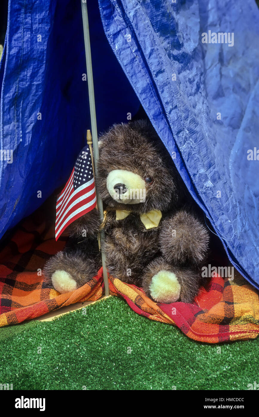 A stuffed bear toy holds an American flag inside a blue tent on Independence Day in the USA. Stock Photo