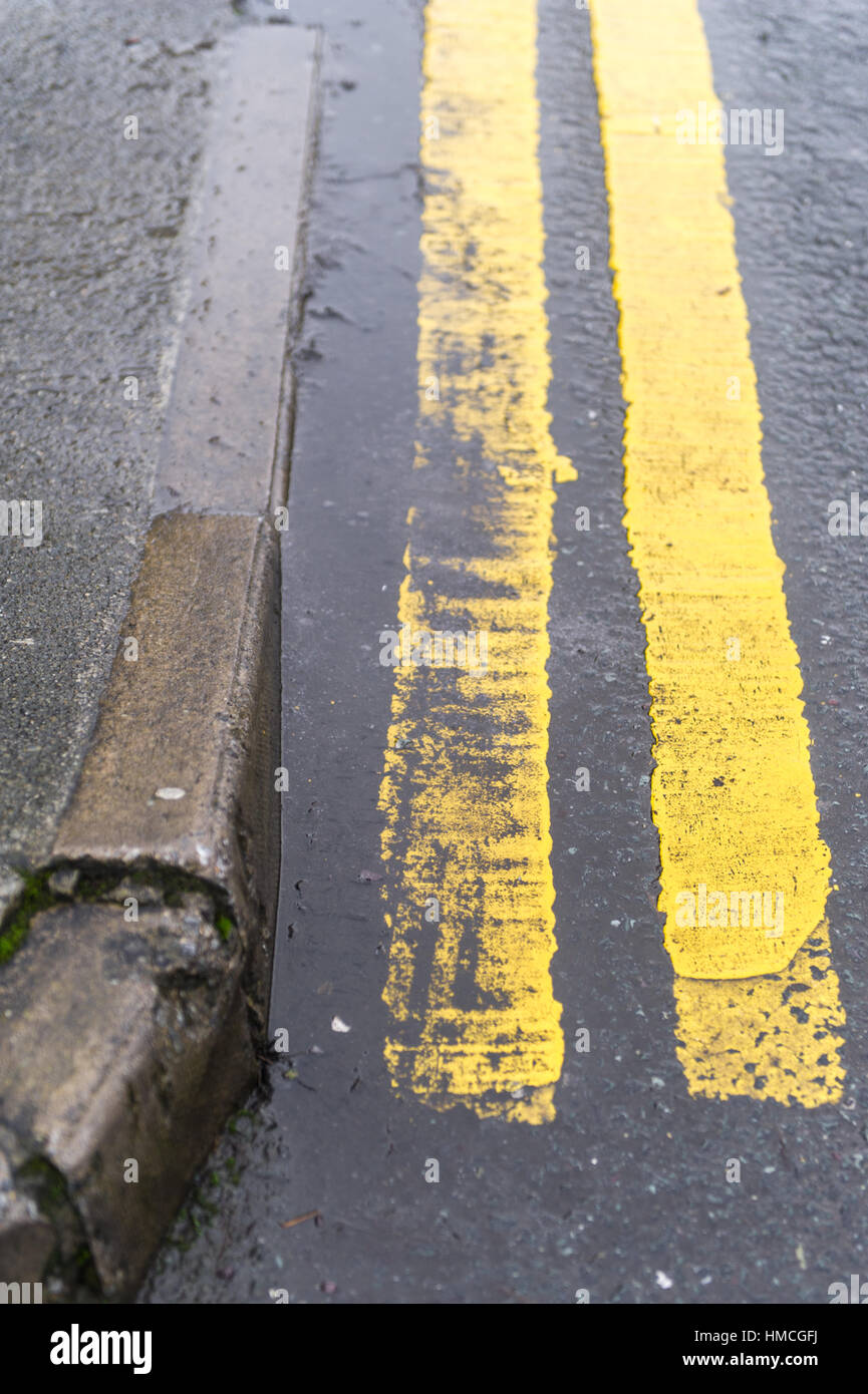 Double yellow lines on a wet road next to a kerb with copy space. Stock Photo