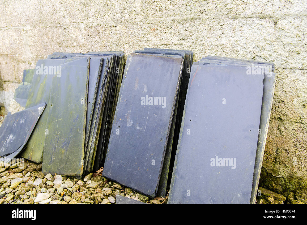 Stack of second hand roof slates/tiles leaning against a breeze block wall. Stock Photo