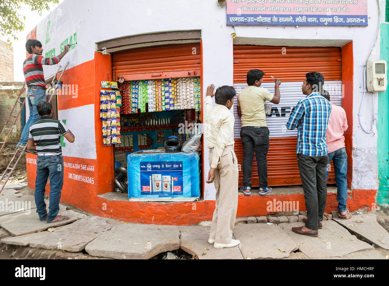 Three Indian men paint a shop front while another three stand watching Stock Photo