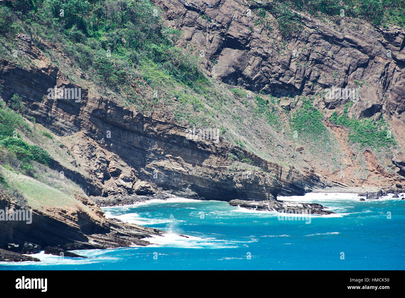 ocean waves hitting big stone rocks on sunny day Stock Photo