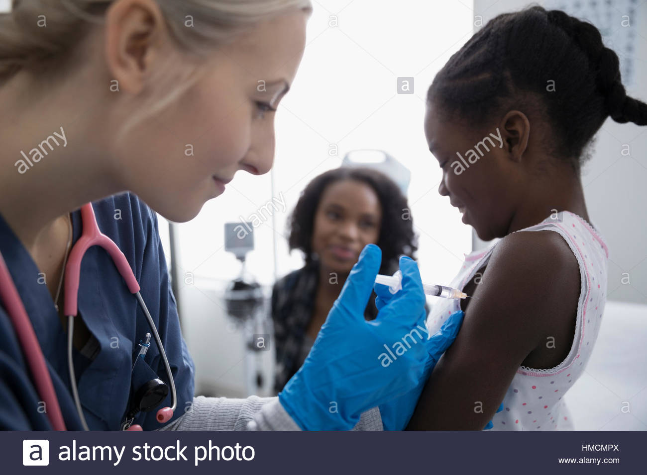 Female nurse giving frightened girl patient an injection in the arm in clinic examination room Stock Photo