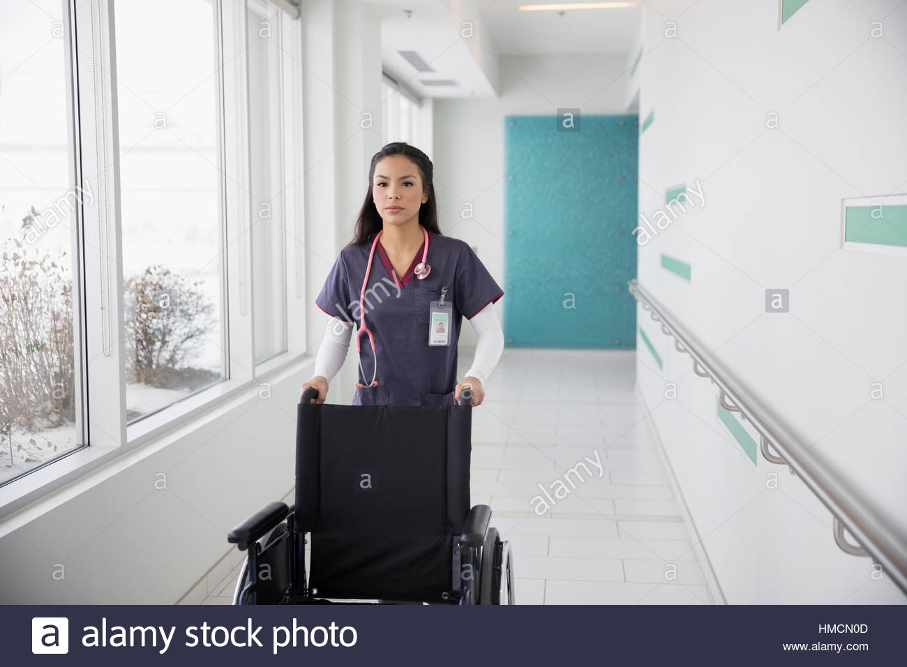 Female nurse pushing wheelchair in clinic corridor Stock Photo Alamy