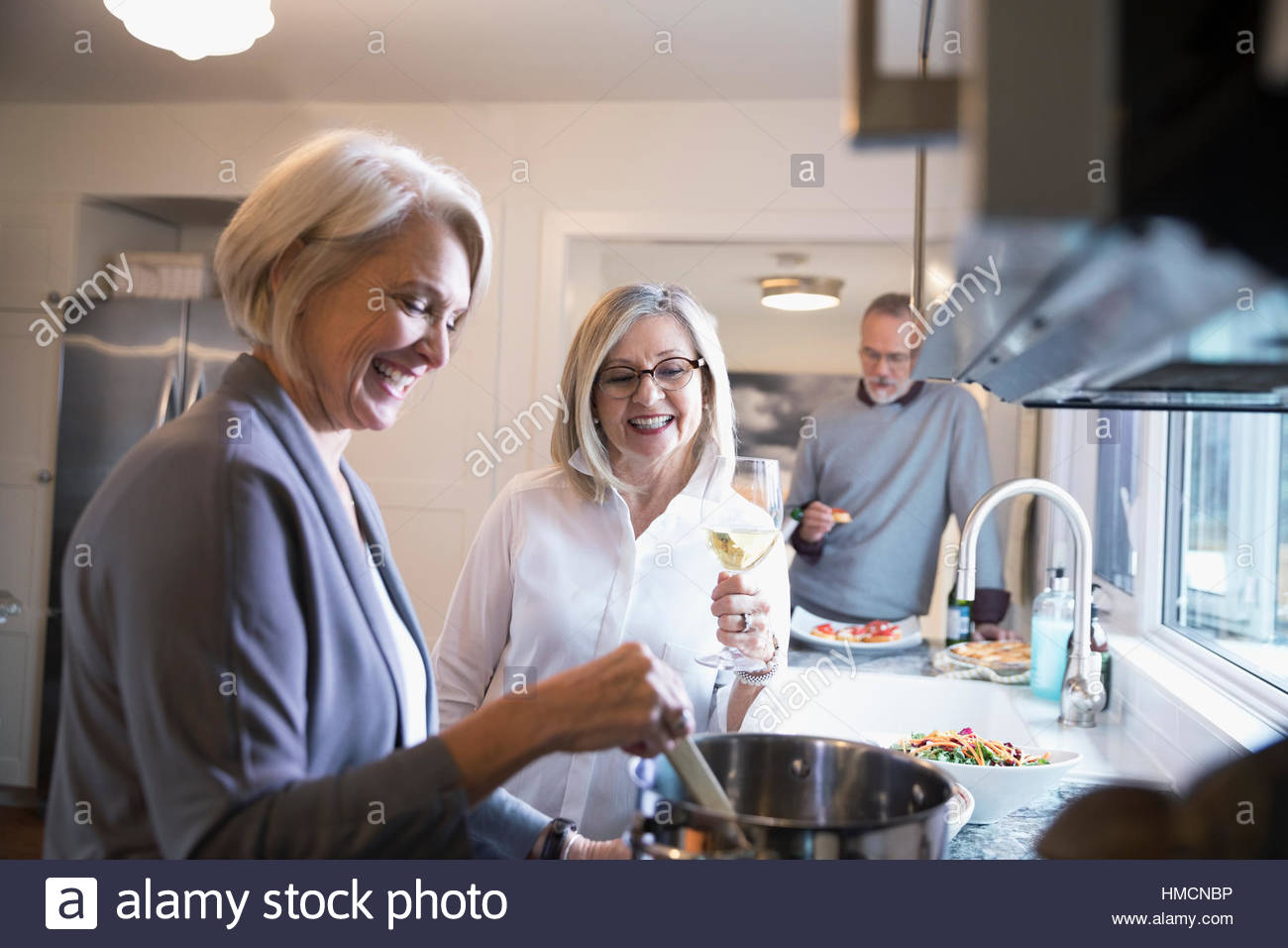 Senior women friends cooking and drinking wine in kitchen Stock Photo