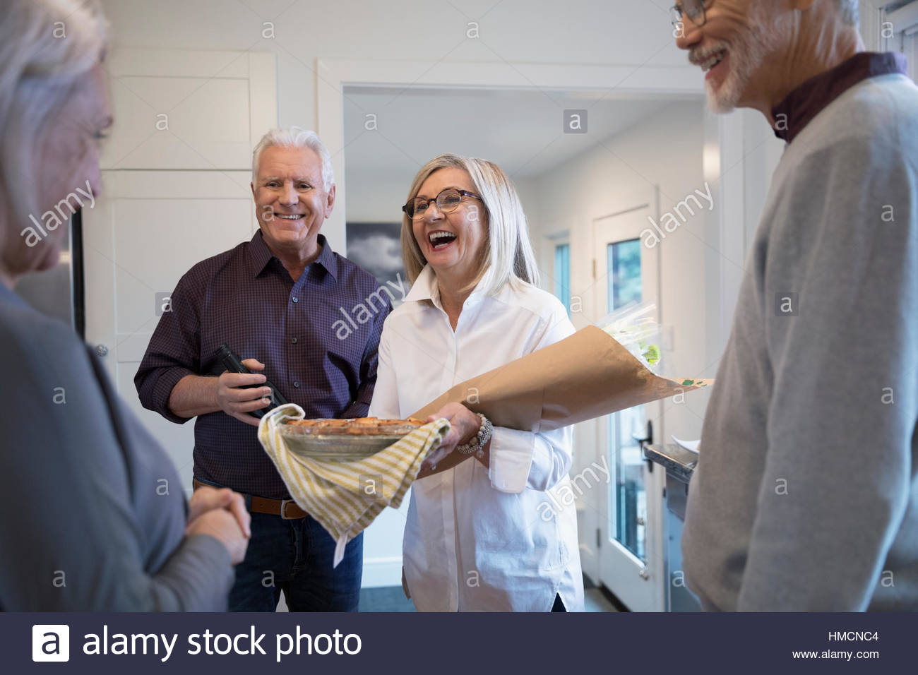Senior couple with flowers and pie arriving at dinner party Stock Photo