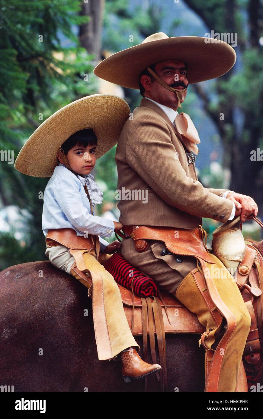 Boy and man on horseback wearing traditional clothes and wide-brimmed hats, Mexico. Stock Photo