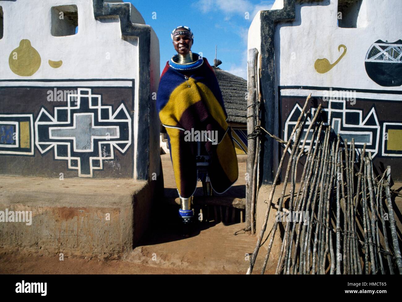 Ndebele man wearing a traditional costume at the entrance to a house with decorated walls, South Africa. Stock Photo