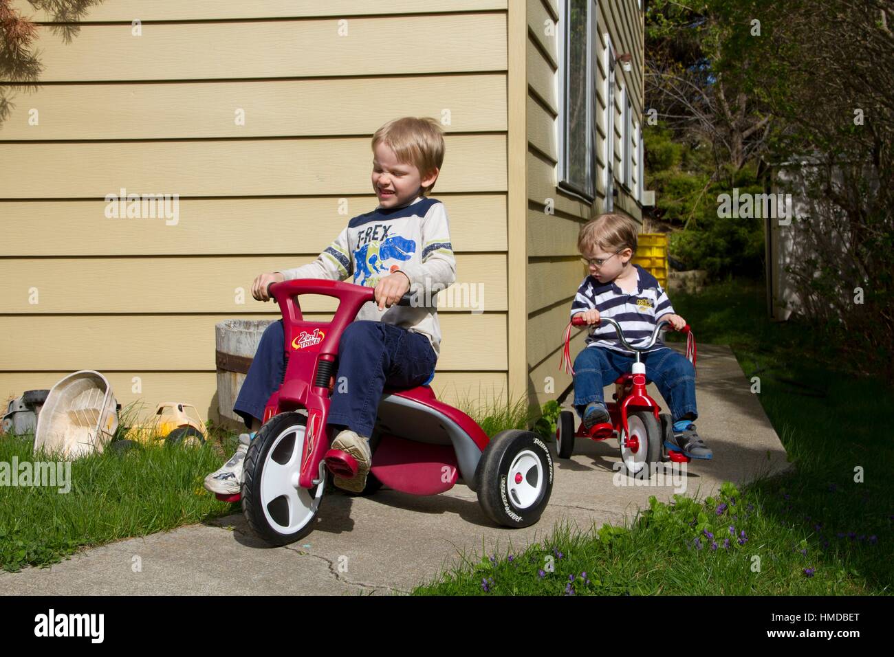 Two boys ride trikes outdoors. Stock Photo