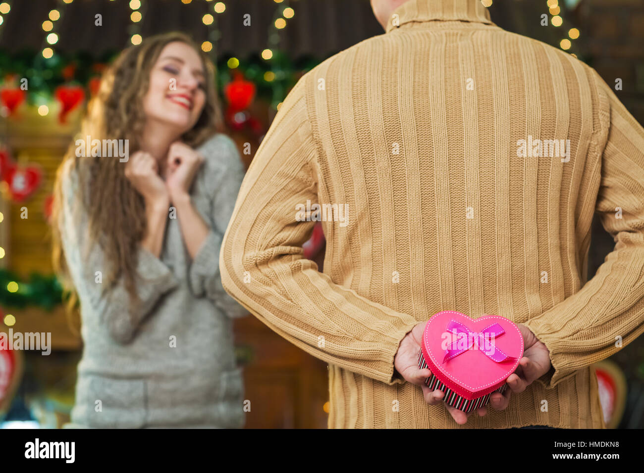 Man holding gift in hands behind his back, pink box with heart-shaped with purple bow. girl with impatient waiting gift Stock Photo