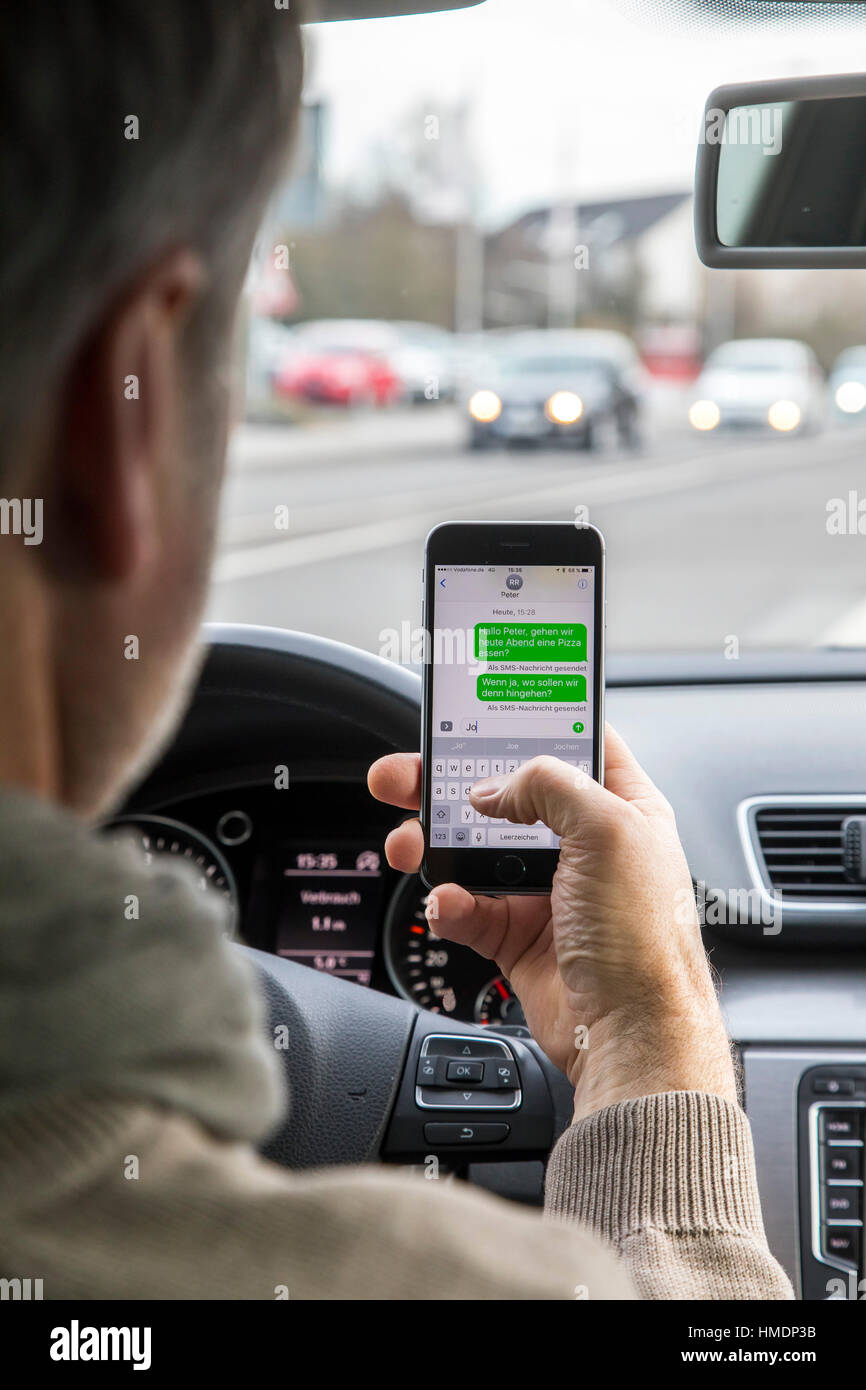 A car driver is using a mobile phone, smartphone, while driving the car