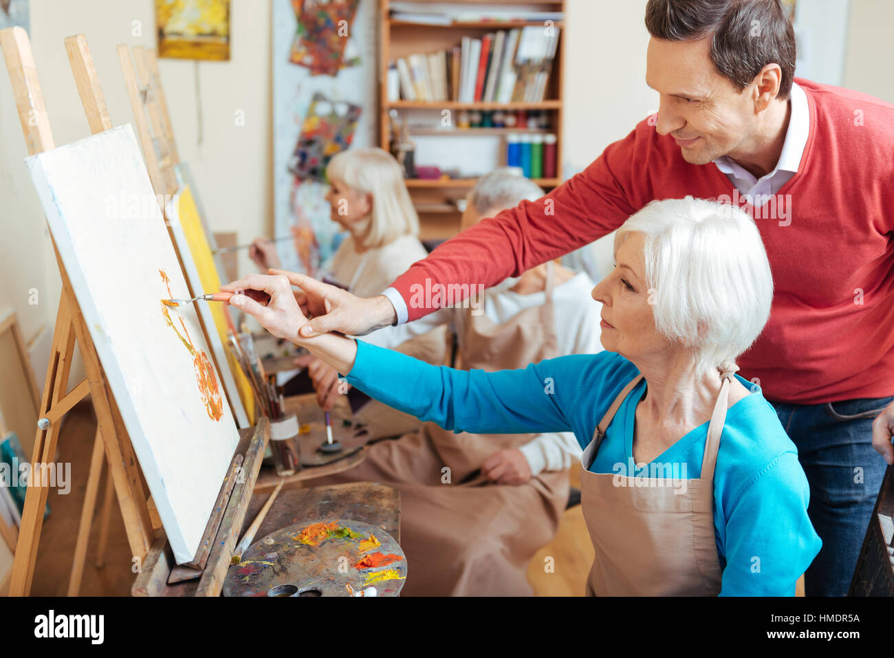 Delighted artist helping elderly woman in painting studio Stock Photo